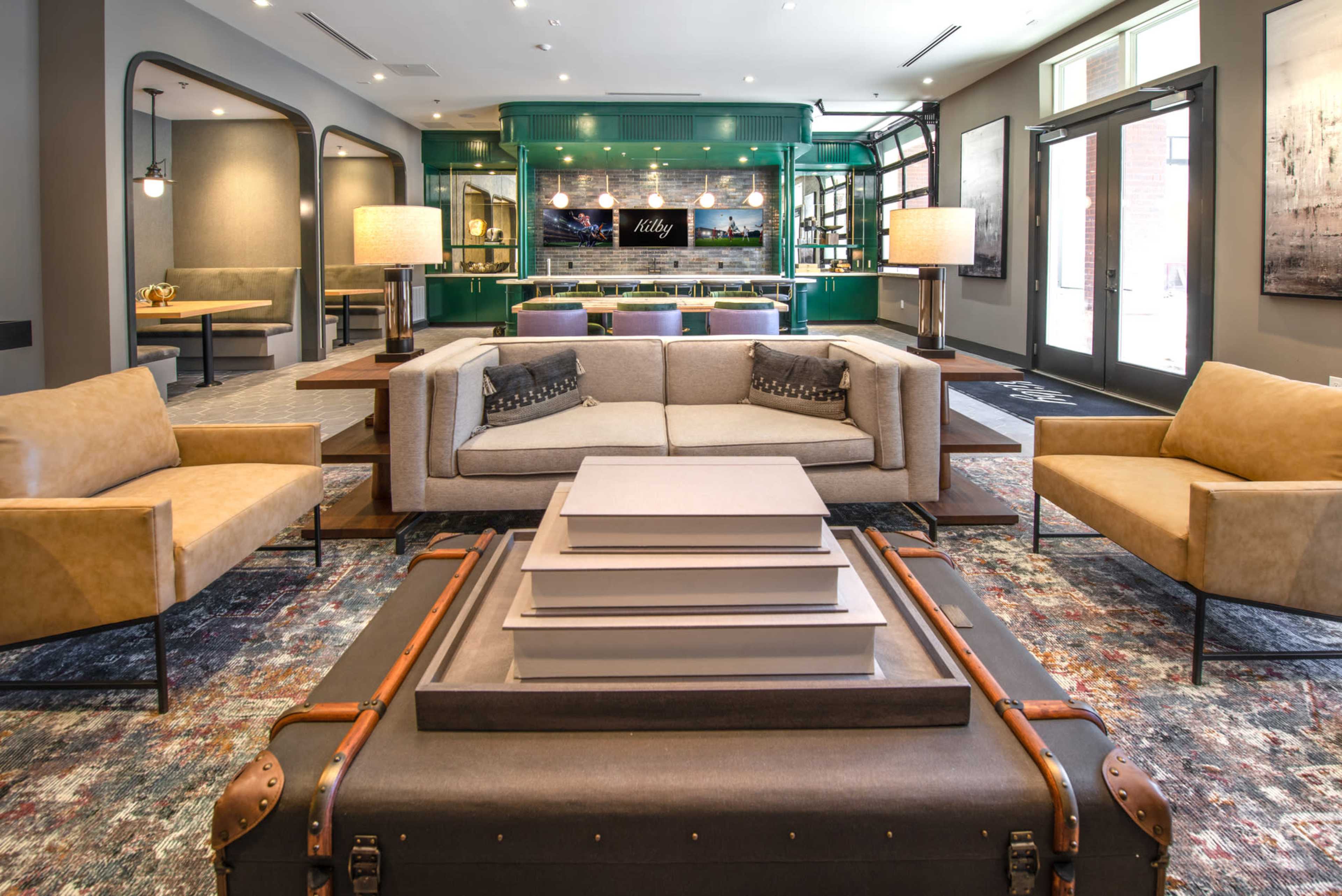 A modern lounge area featuring a large sofa, two armchairs, and a central coffee table, with a green accent wall and large windows.