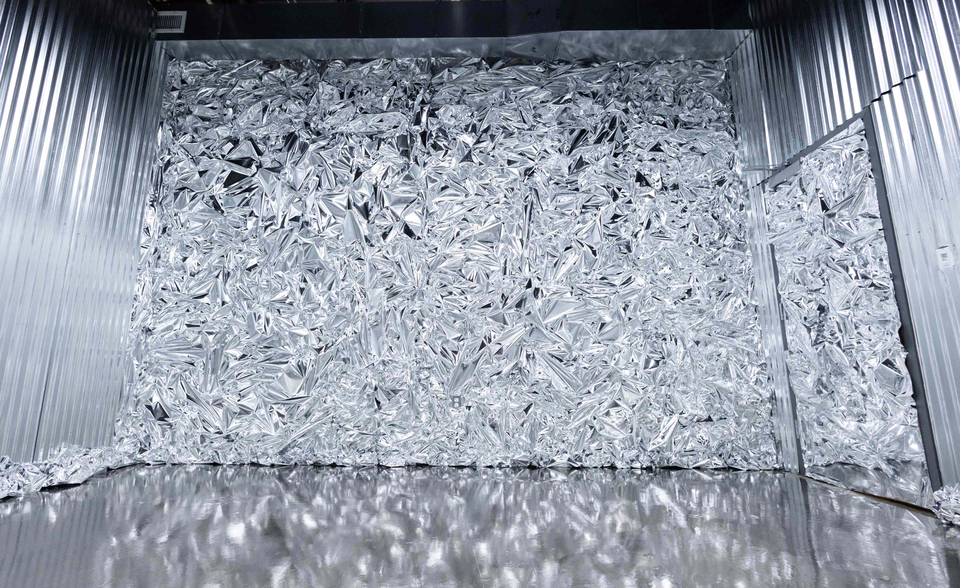 A wall covered in crumpled silver foil with a reflective floor beneath it.