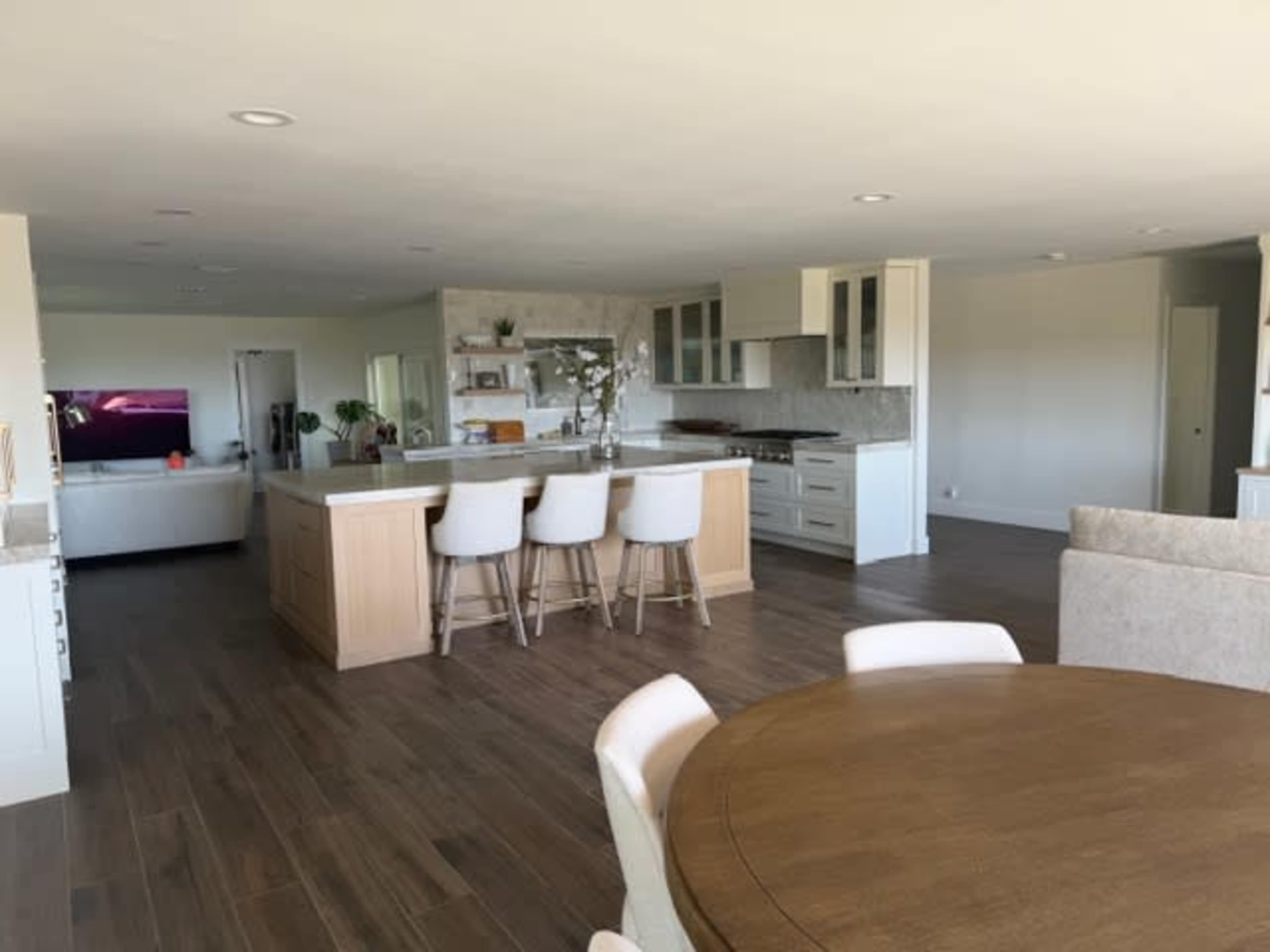The image shows a spacious, modern open-concept kitchen and living area with a large island, bar stools, and a dining table.
