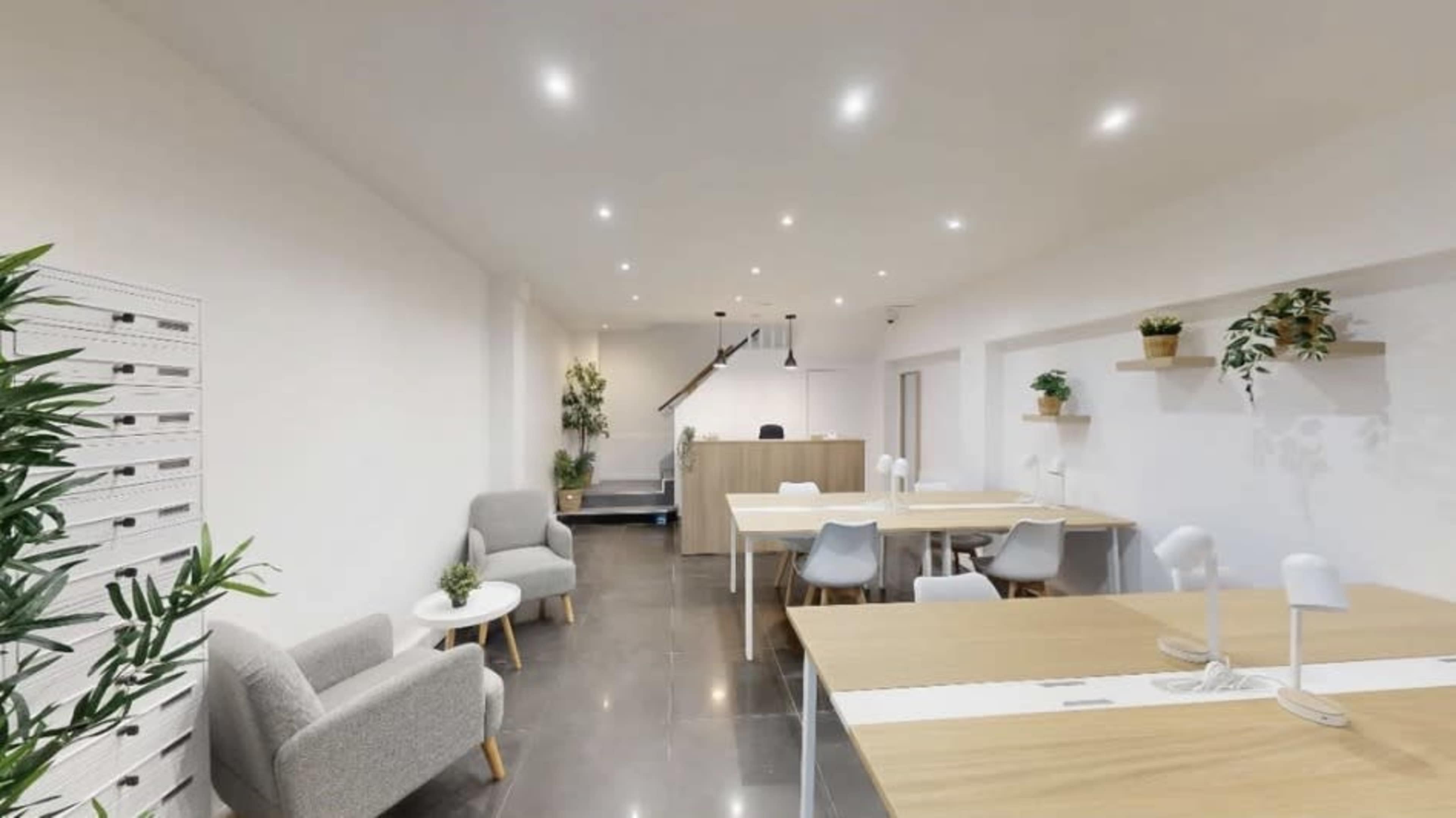 The image shows a modern office space with tables, chairs, and plants, featuring neutral-colored walls and bright lighting.