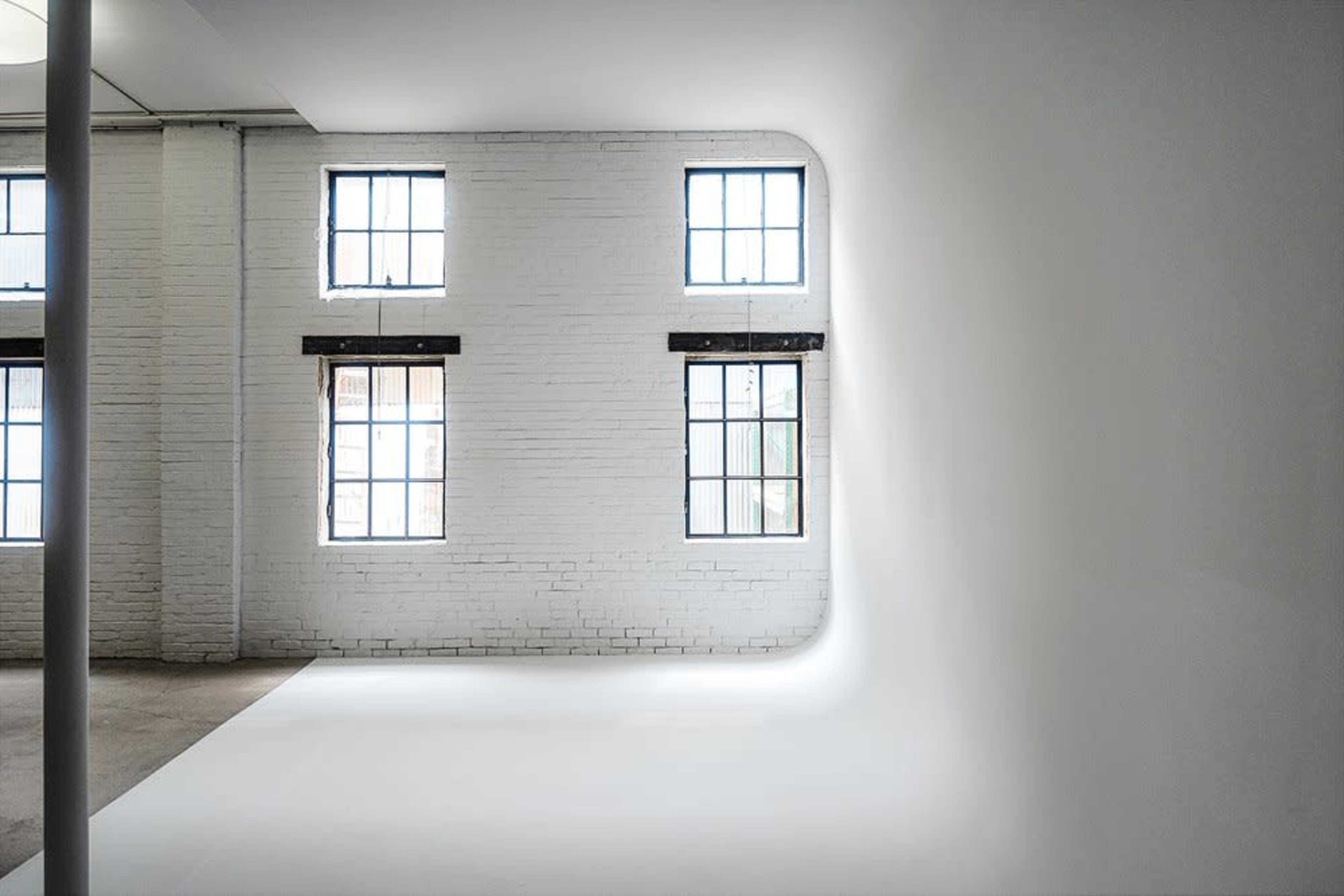 A minimalist interior space with white walls and large windows illuminating the room.