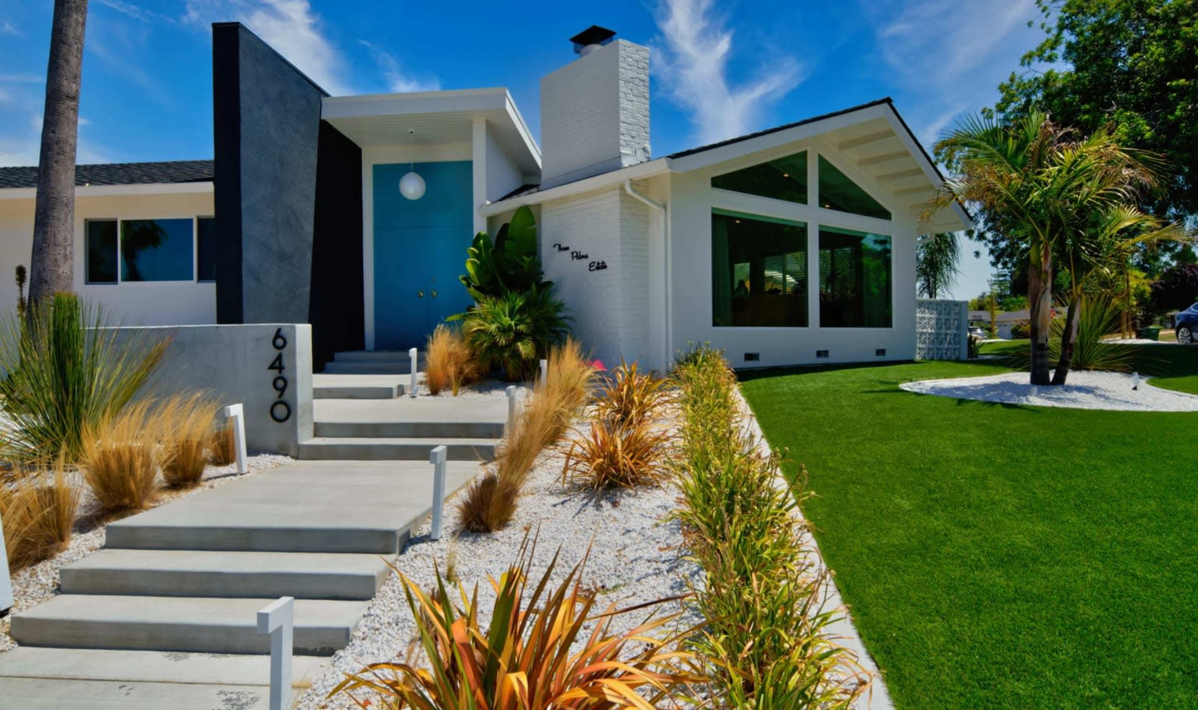A modern residential house with a mix of white and gray exterior, featuring a landscaped front yard with grasses and decorative rocks.