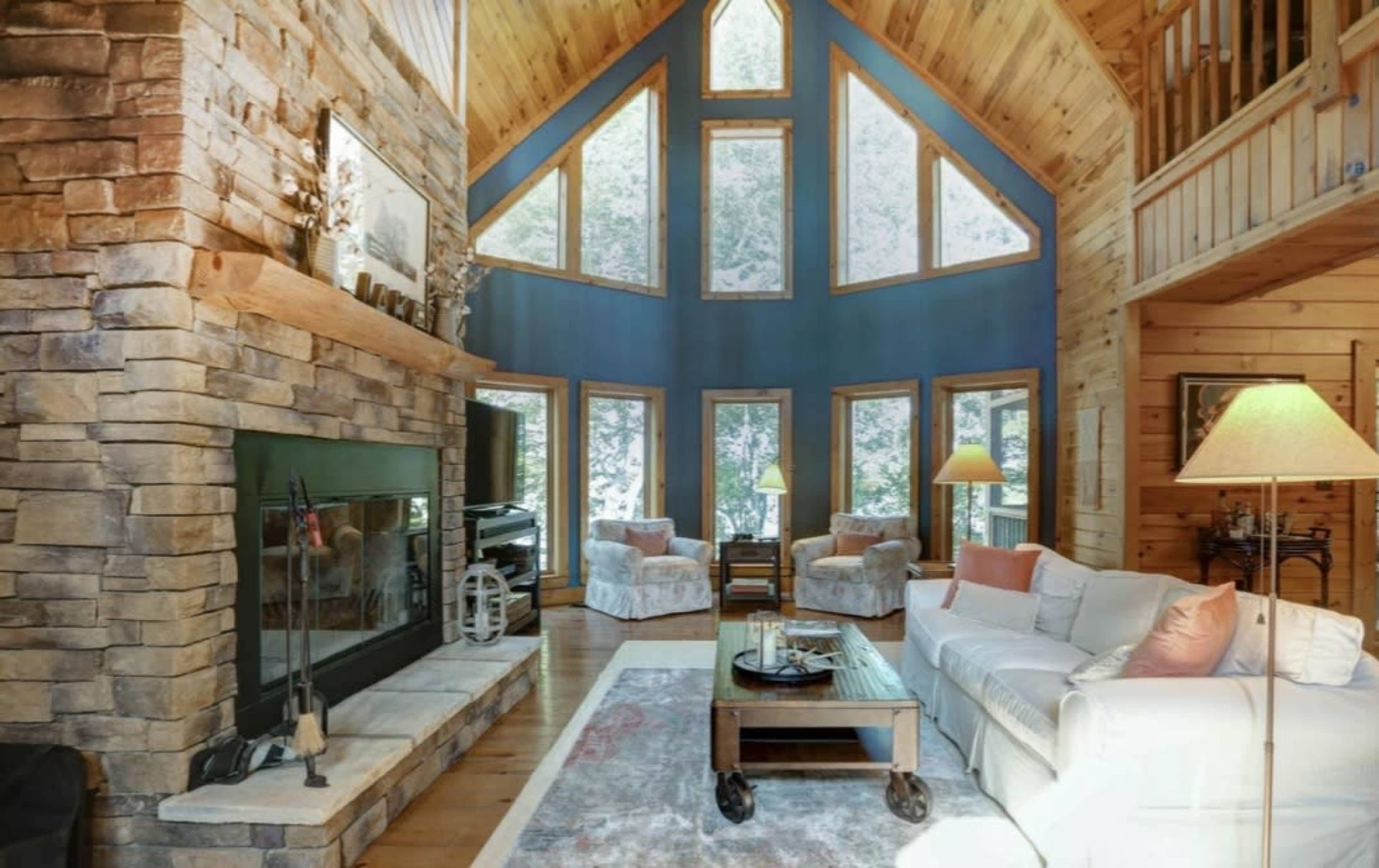 A spacious living room with high ceilings, a stone fireplace, large windows, and wooden accents.