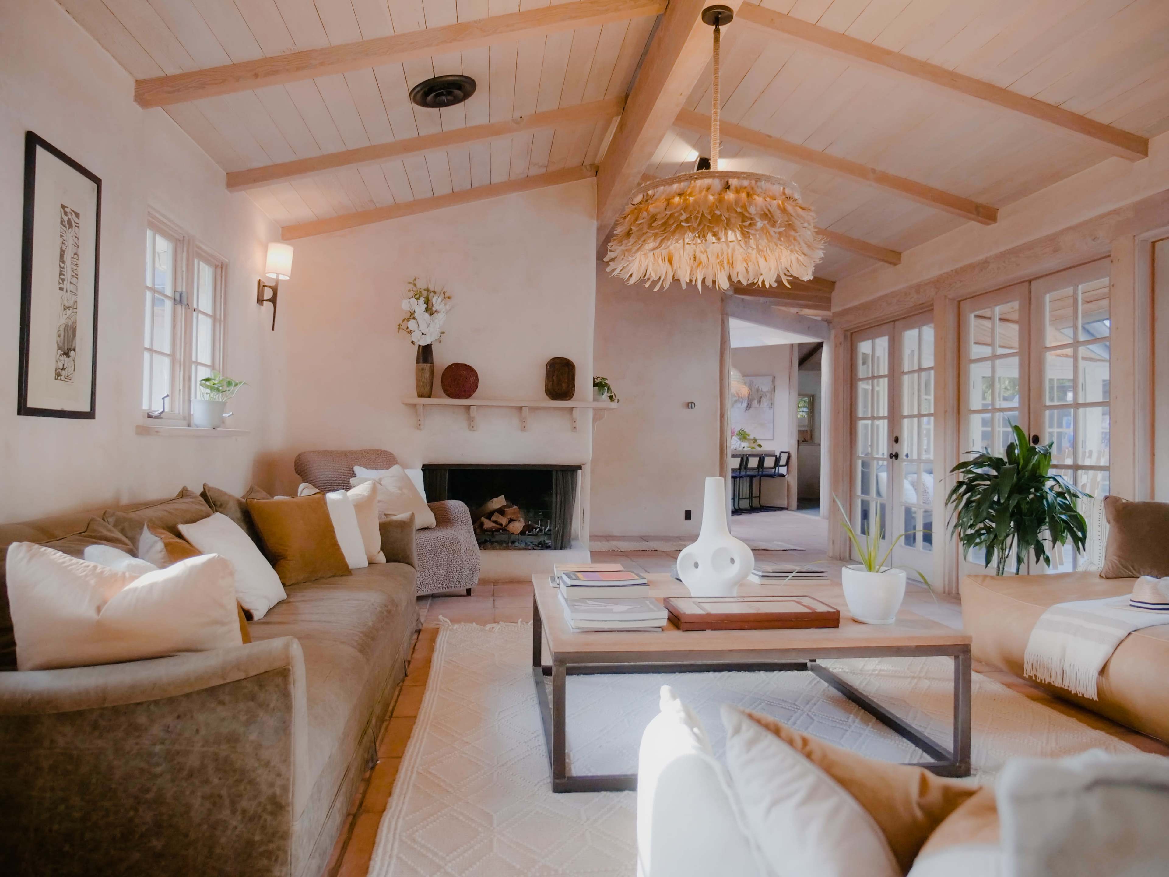 A cozy living room with a large sofa, a coffee table, and a decorative ceiling light, featuring a fireplace and windows leading to an outdoor space.