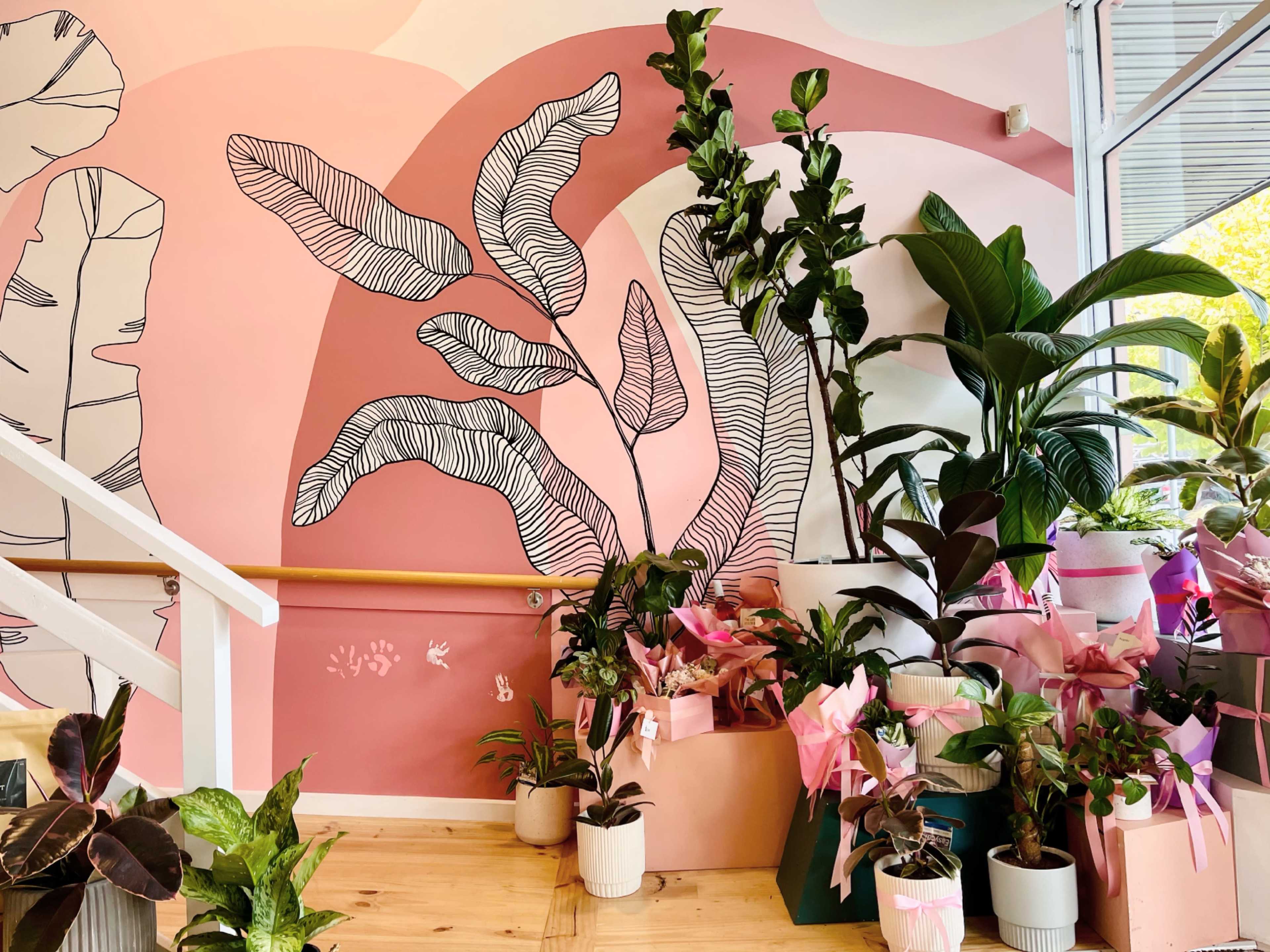 A staircase adorned with a pink and white mural featuring large leaves, surrounded by various potted plants with decorative wrappings.