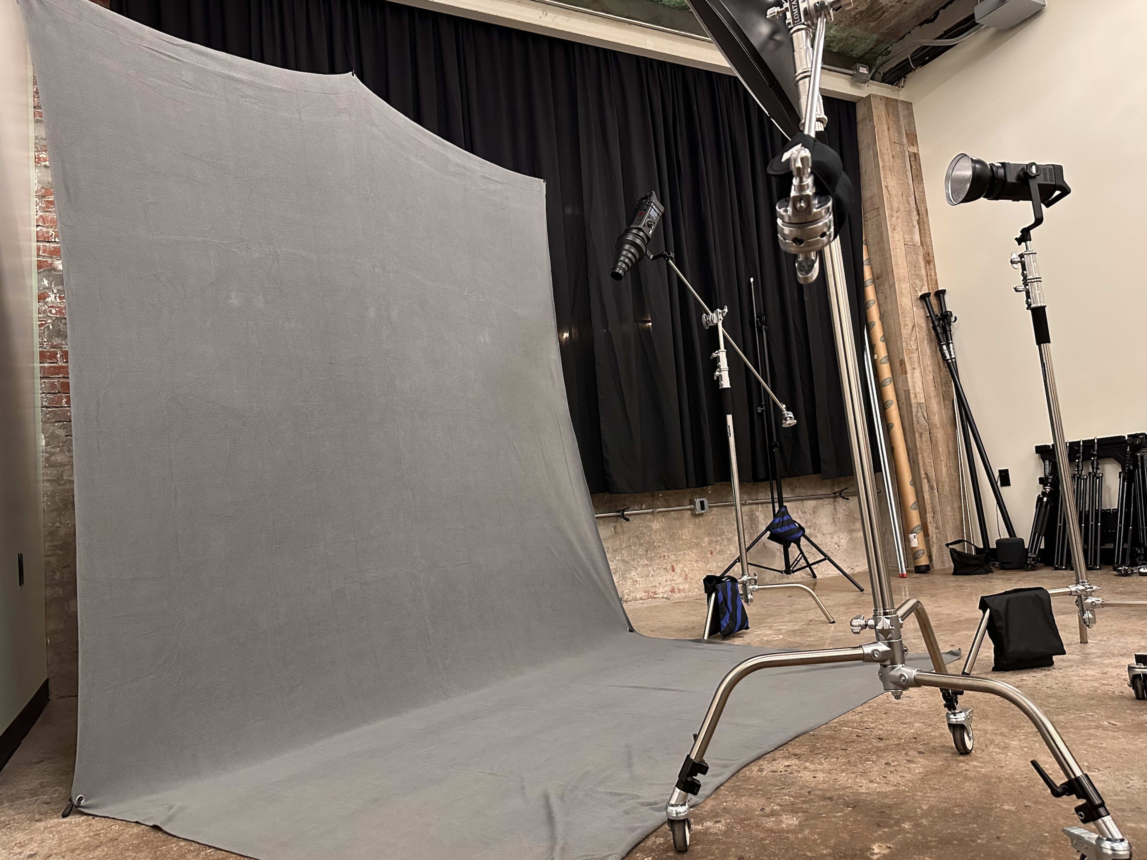 A photography studio with a grey backdrop, lighting equipment, and various support stands.