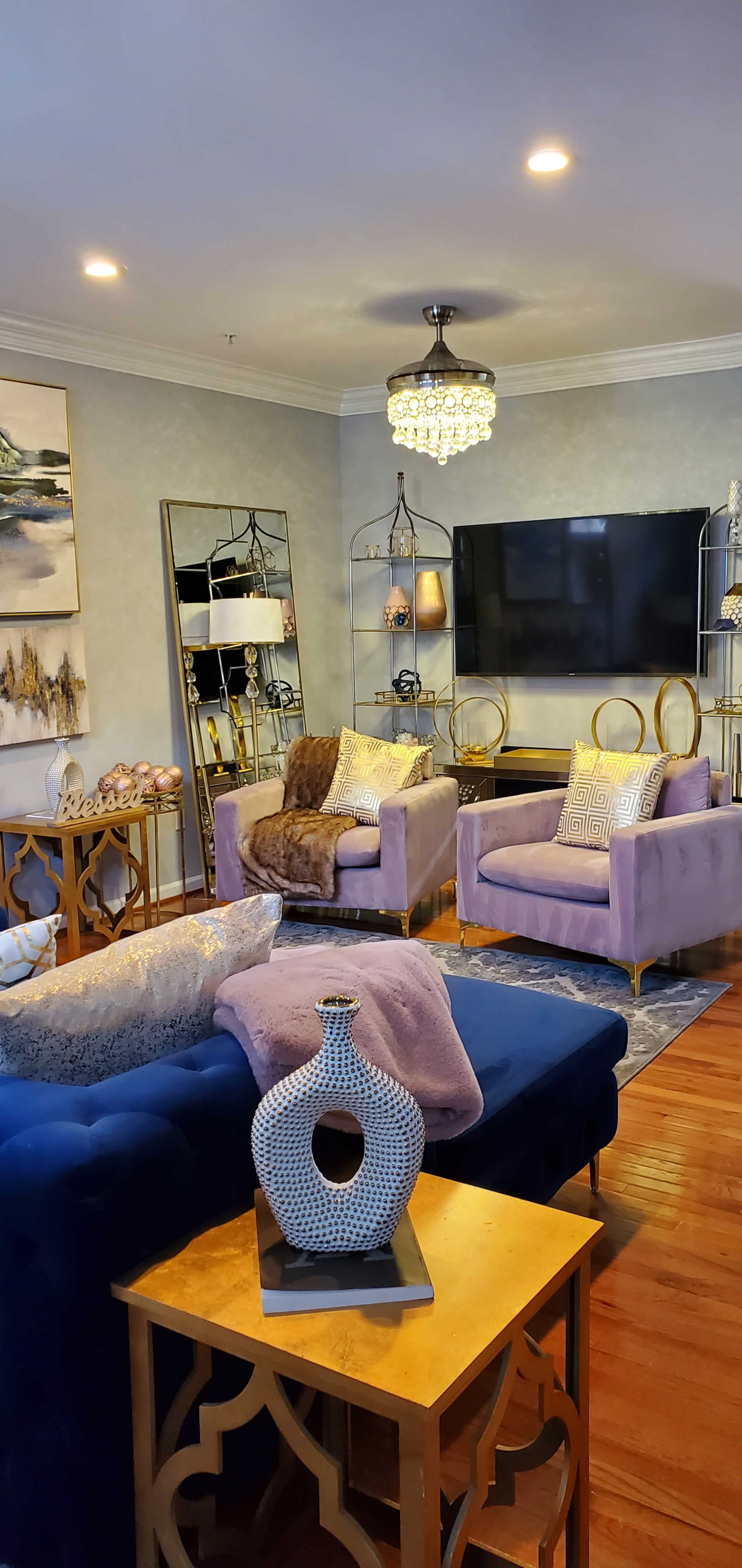 The living room features two purple chairs, a blue sofa, a large mirror, and a mounted television against a light blue wall.