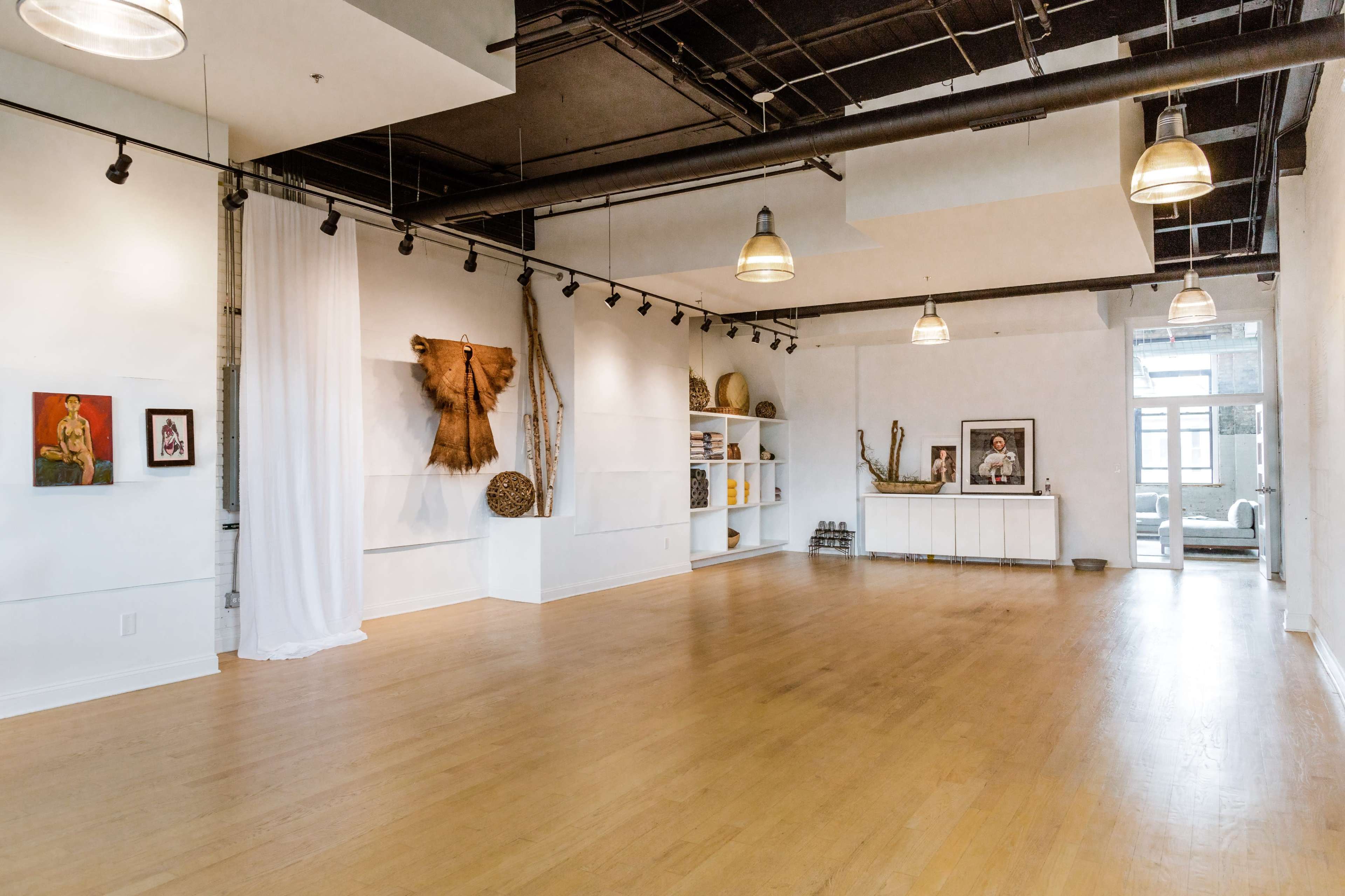 A spacious, well-lit room with wooden floors, art on the walls, and a minimalist white shelf arrangement.