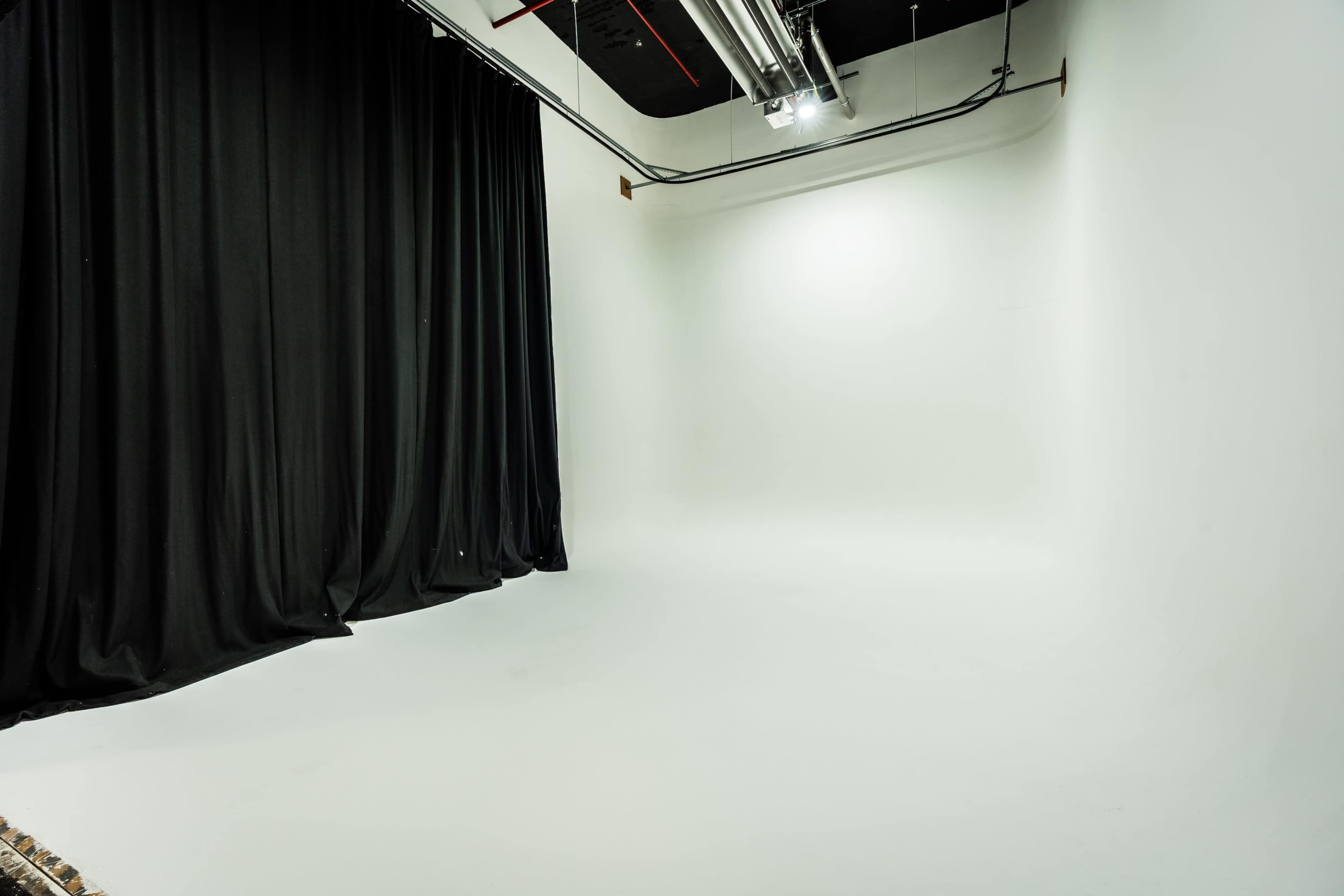 The image shows a spacious photography studio with white walls and a large black curtain on one side.