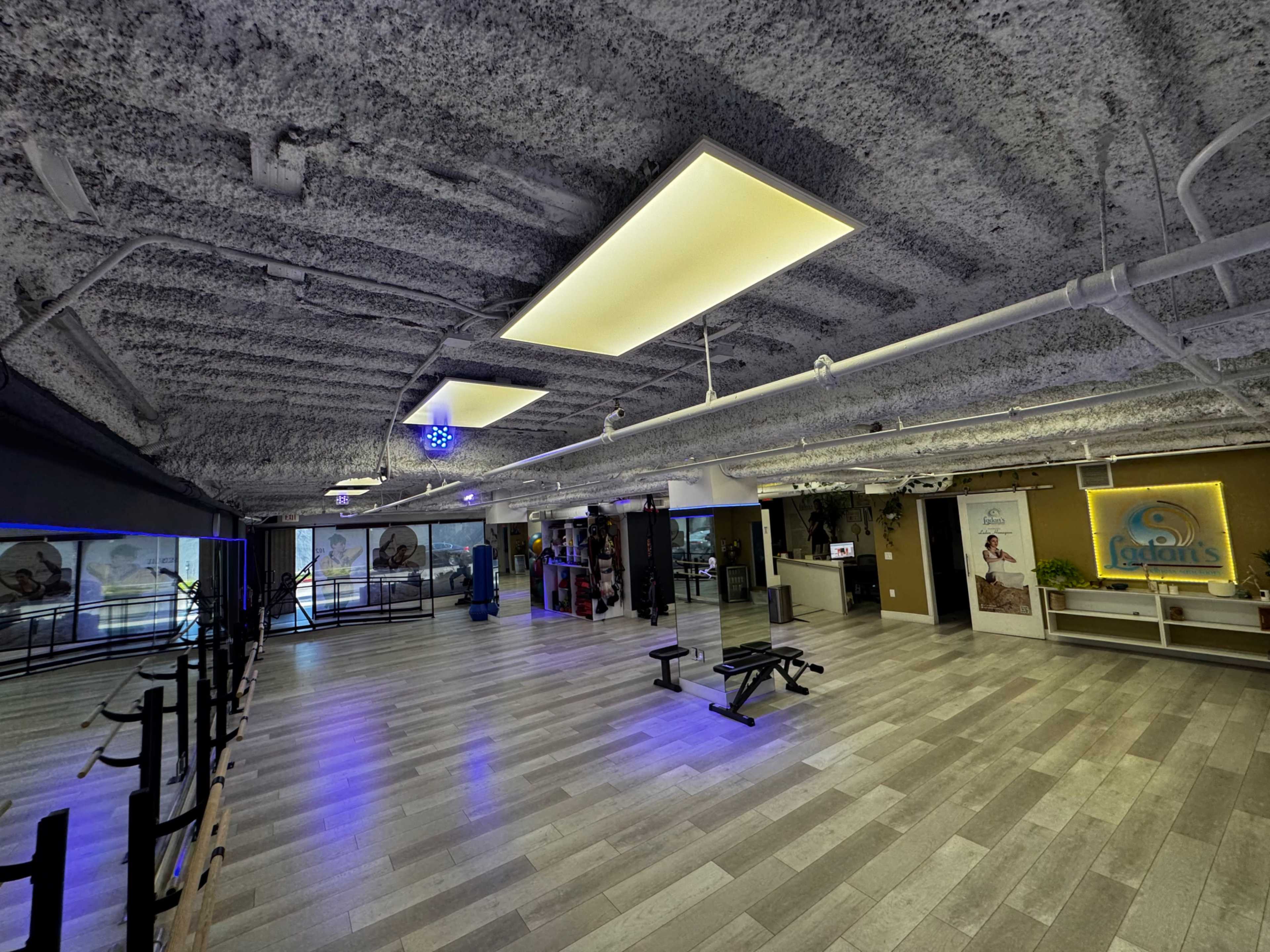 The image shows a spacious fitness center with a textured ceiling, modern lighting, and a variety of exercise equipment arranged on a polished floor.