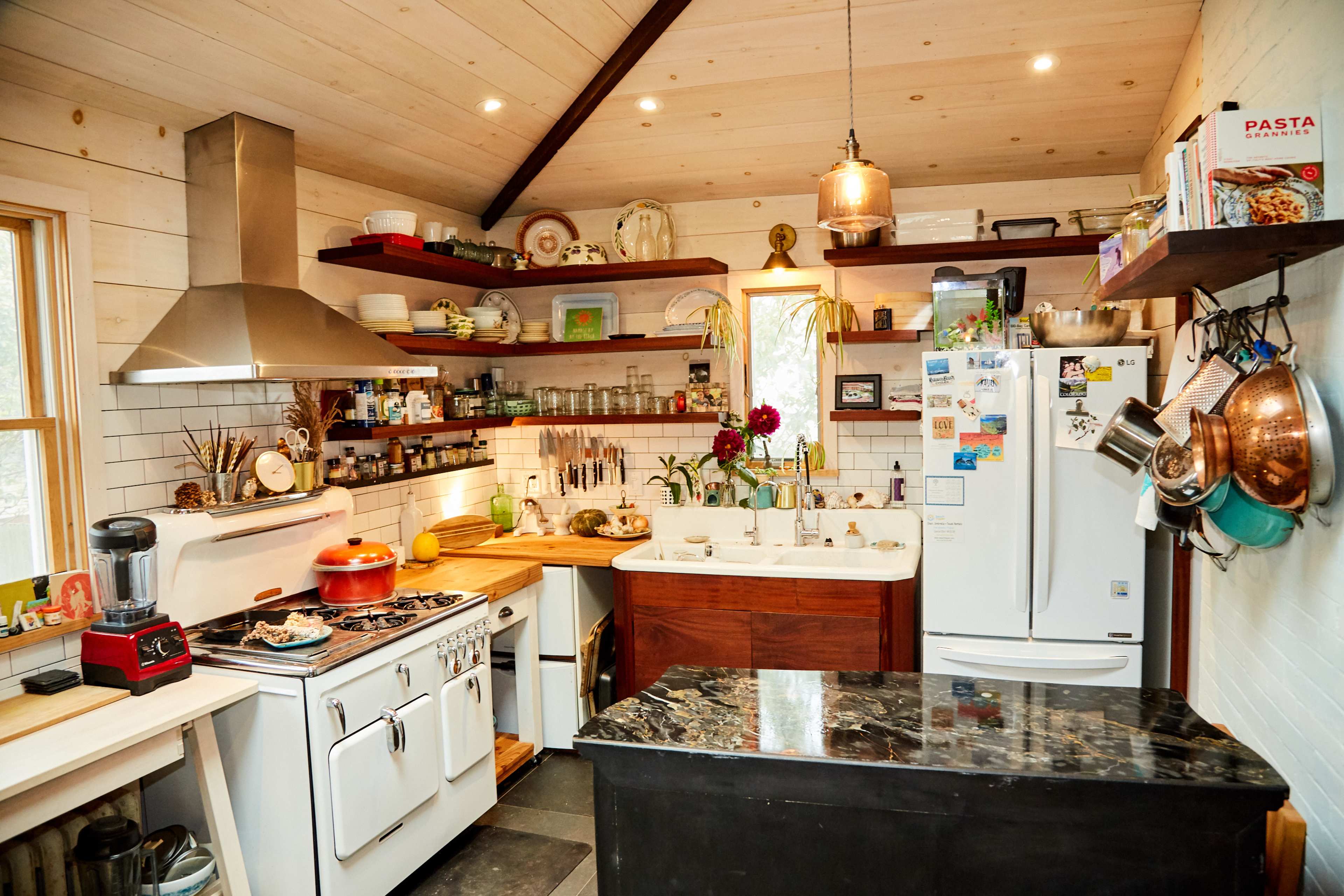 A compact kitchen features a stainless steel stove, a double sink, wooden countertops, and shelves lined with jars and cookware.
