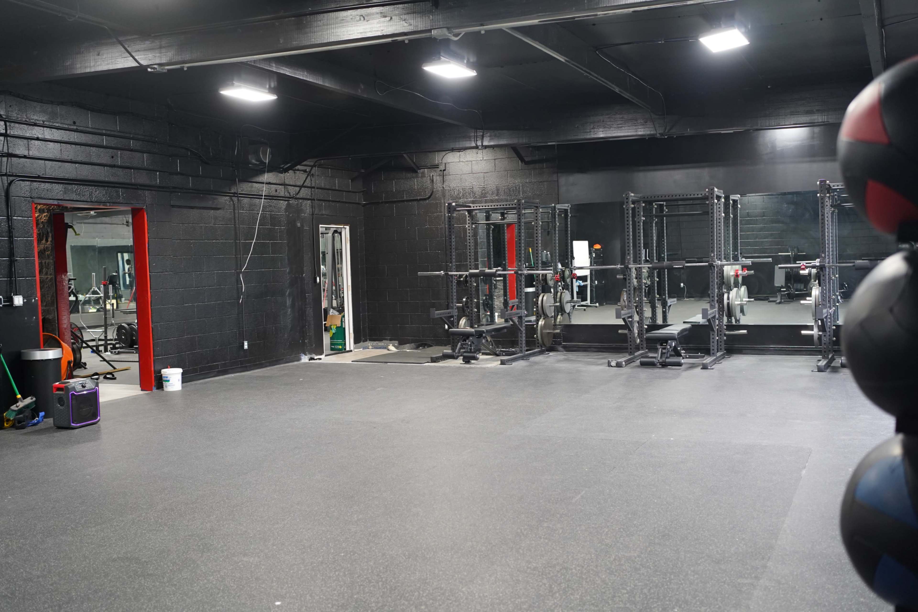 A spacious gym interior with black walls, weightlifting equipment, and mirrored sections reflecting the setup.