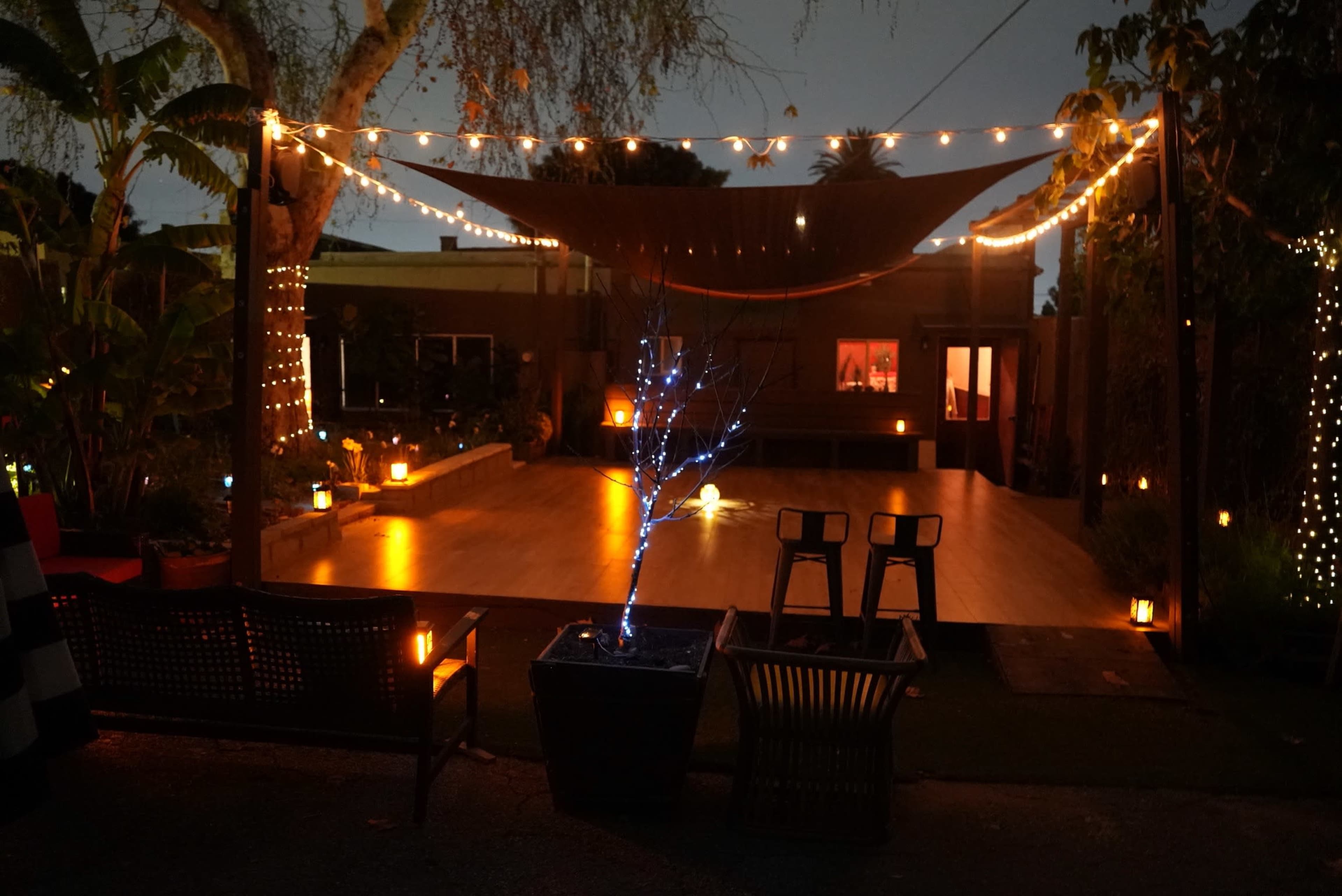 A dimly lit outdoor patio with string lights, a small illuminated tree, and seating arrangements.