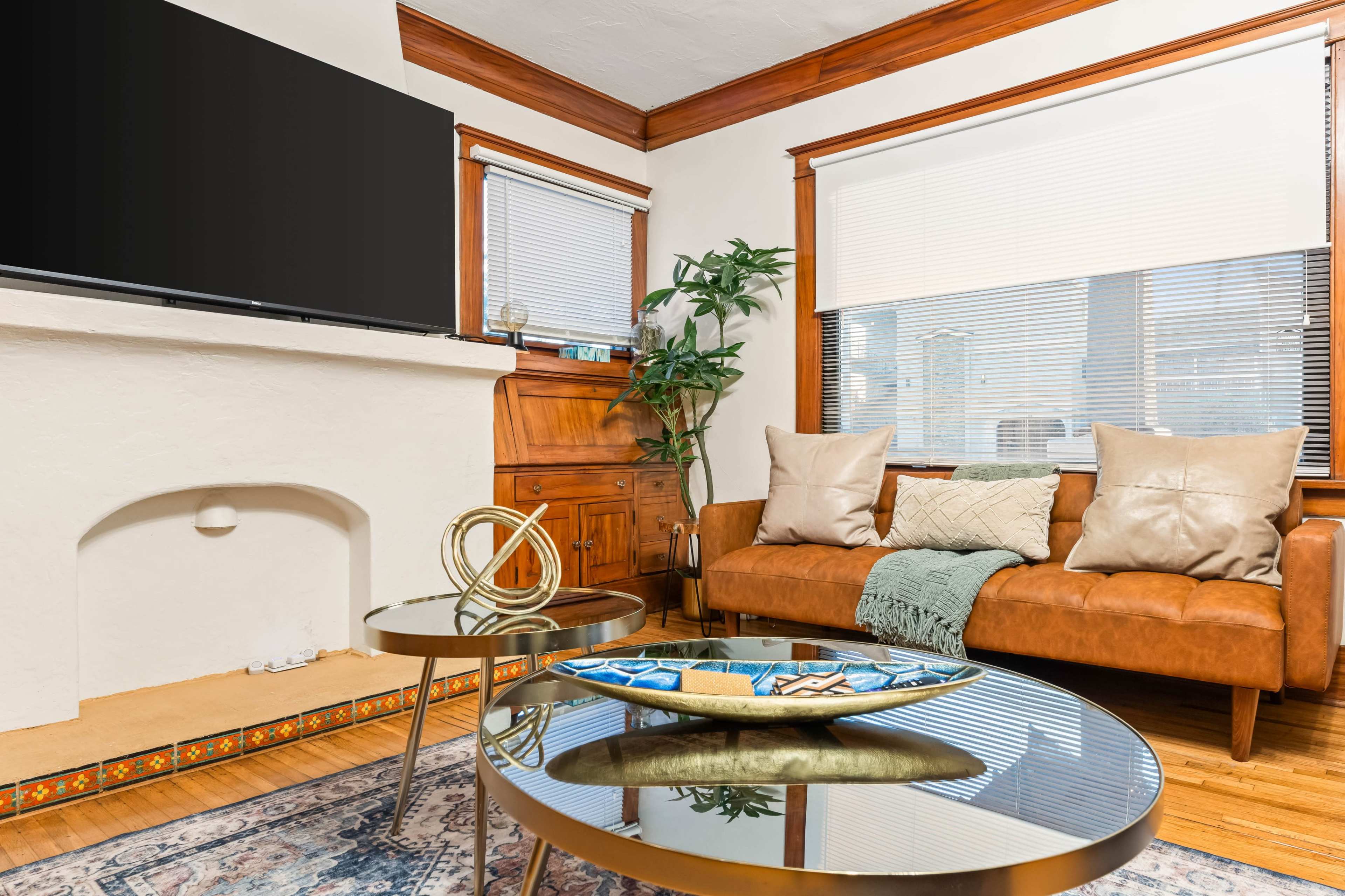 The living room features a leather couch, a decorative coffee table, a potted plant, and a television mounted on the wall above a fireplace.