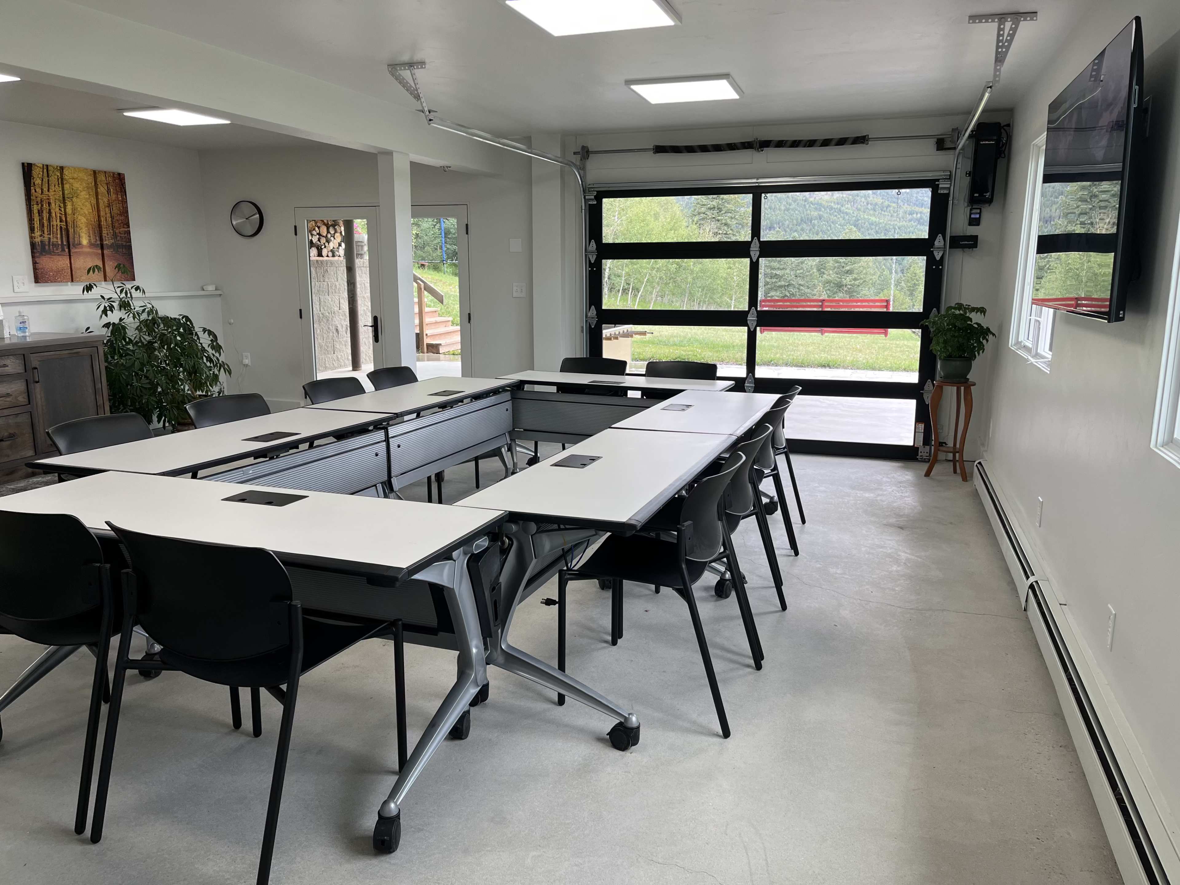 A modern conference room features a large table with movable sections and several black chairs, along with a glass door opening to a scenic view.