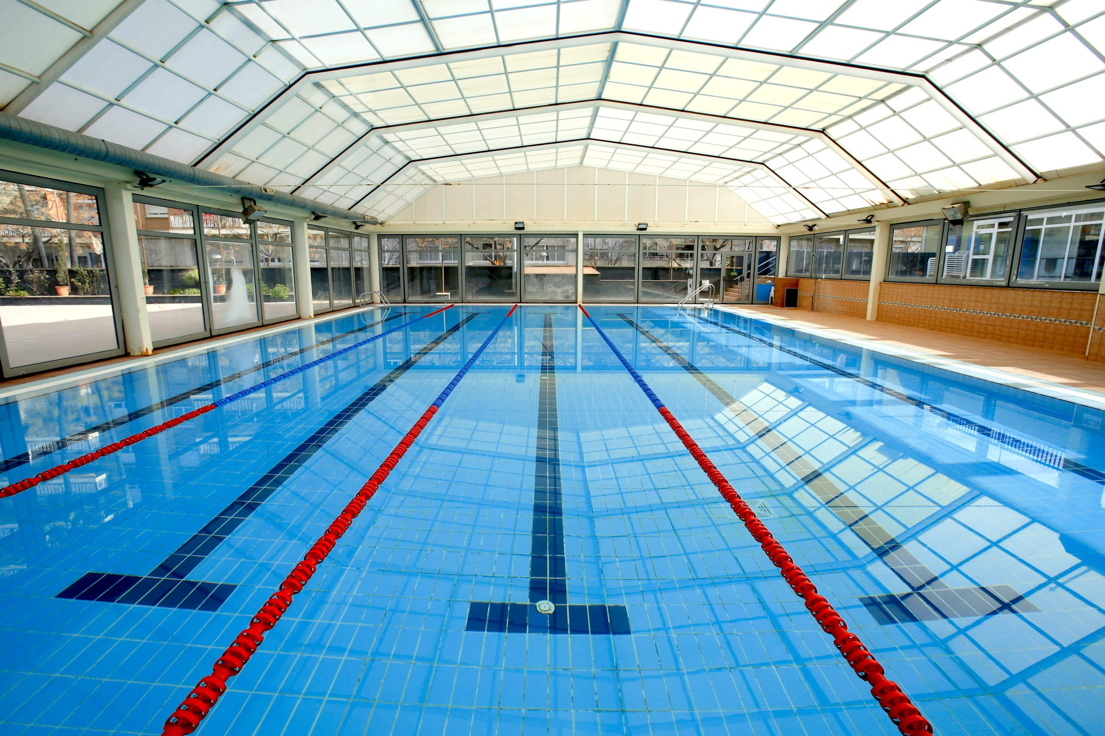 An indoor swimming pool features clear water, lane markings, and a glass roof that allows natural light to enter.
