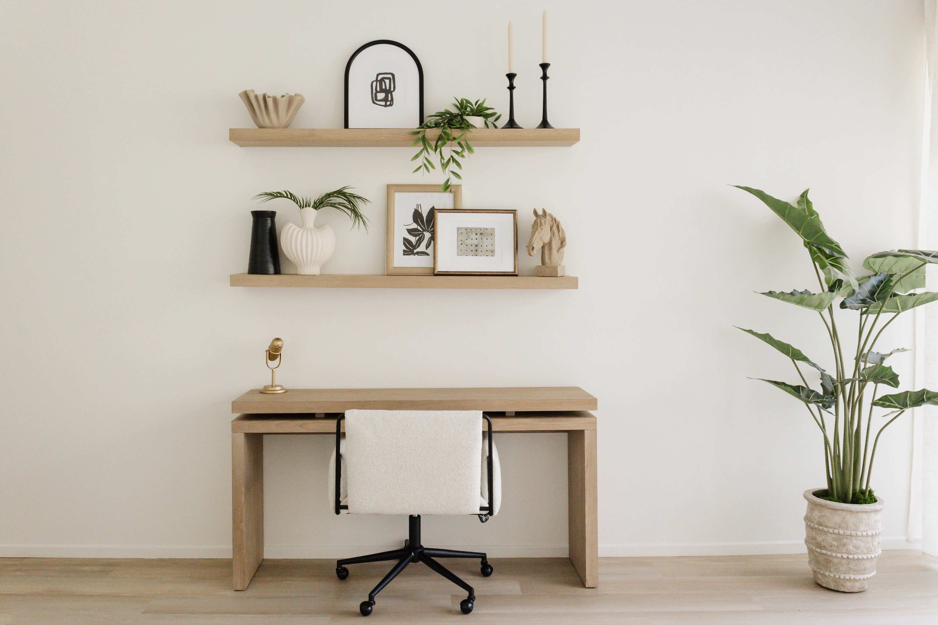 A minimalist workspace features a wooden desk with a chair, flanked by decorative shelves that display various objects and plants against a plain white wall.