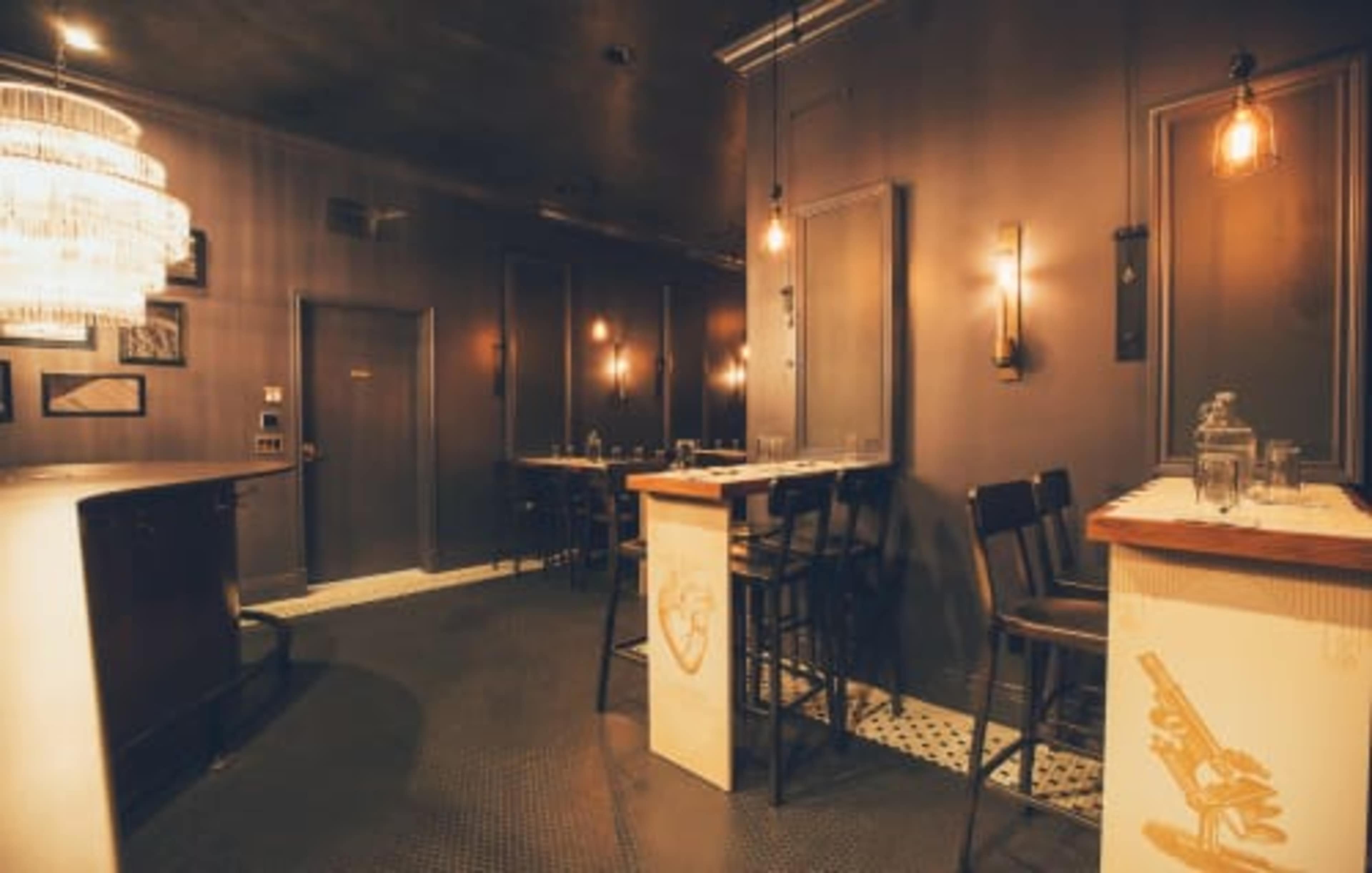 An upscale bar interior with a modern design, featuring dark walls, a sleek counter, and wooden seating.