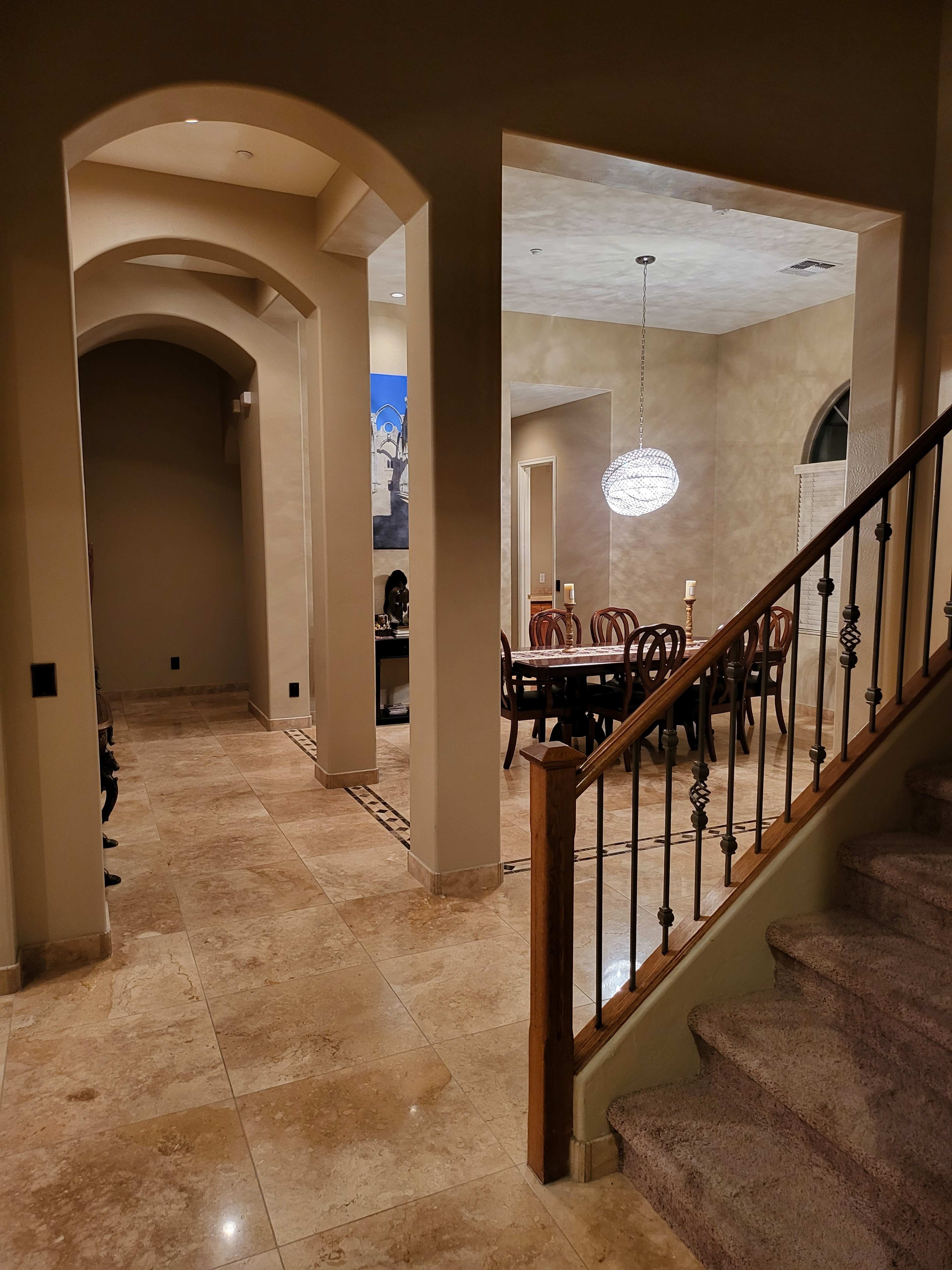 A hallway leading to a dining area with a round chandelier and a staircase on the right.