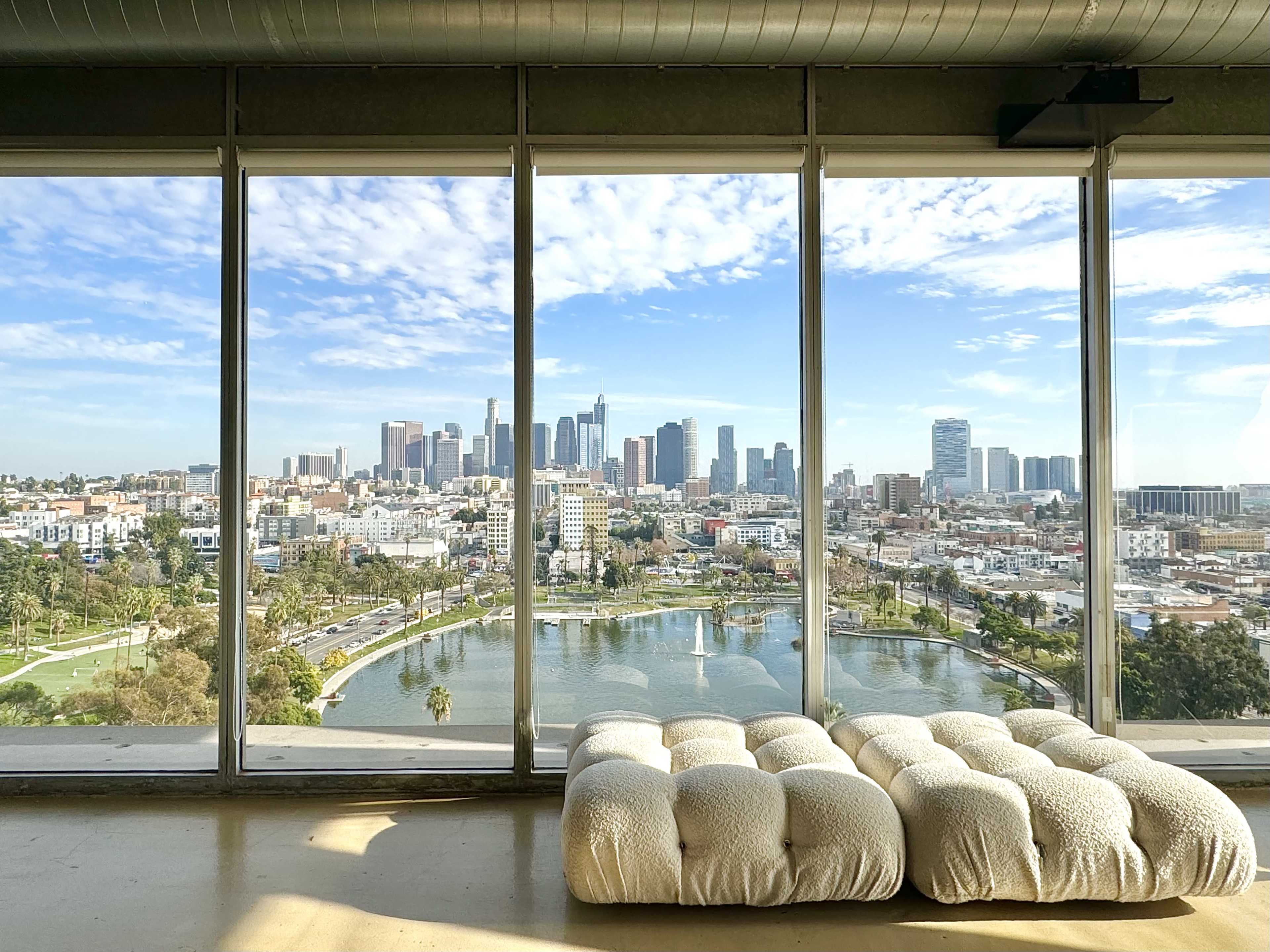 A spacious room with large windows overlooking a city skyline and a park with a lake in the foreground.