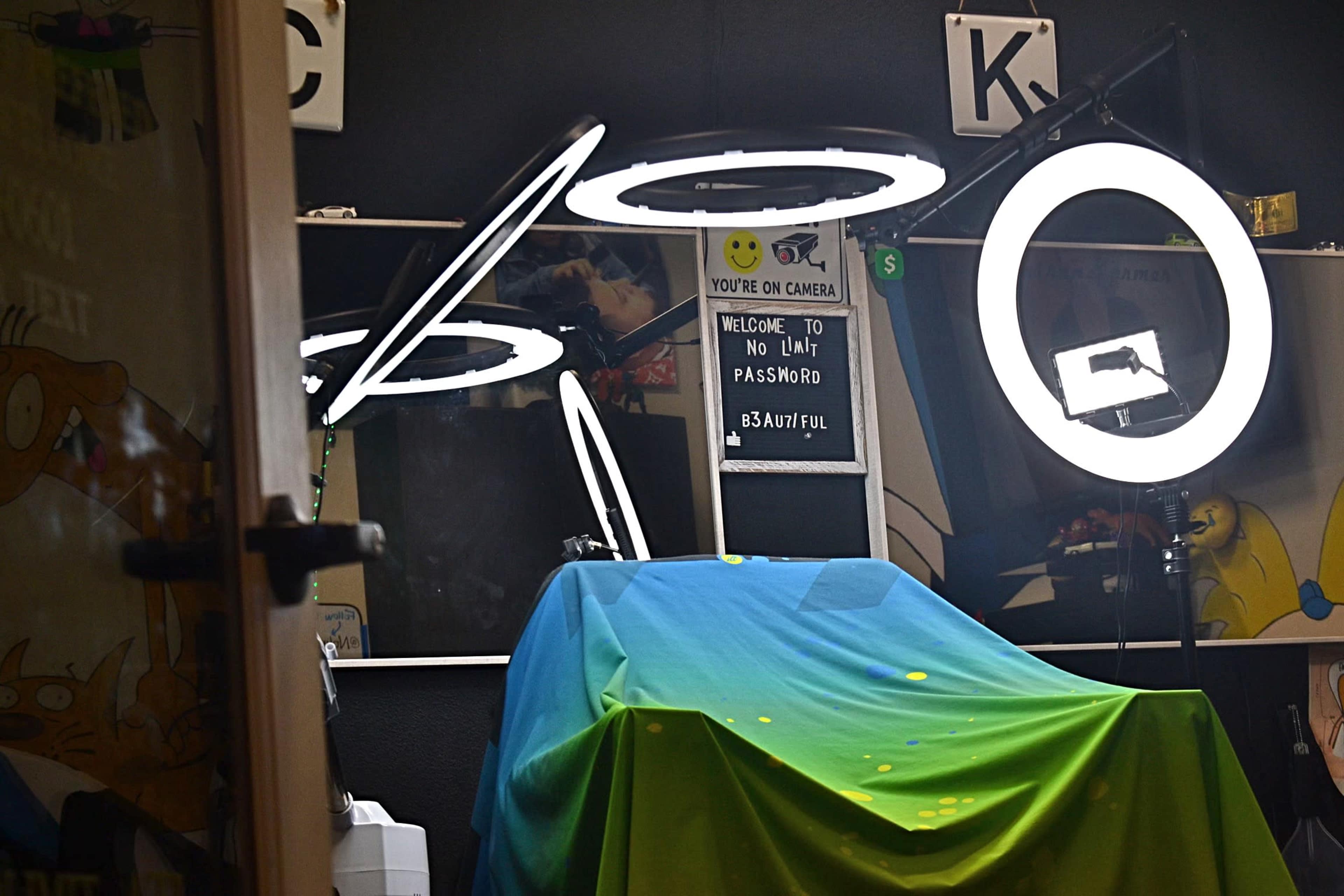 A mysterious room is partially illuminated by ring lights, featuring a covered table and a sign indicating that it is under surveillance.