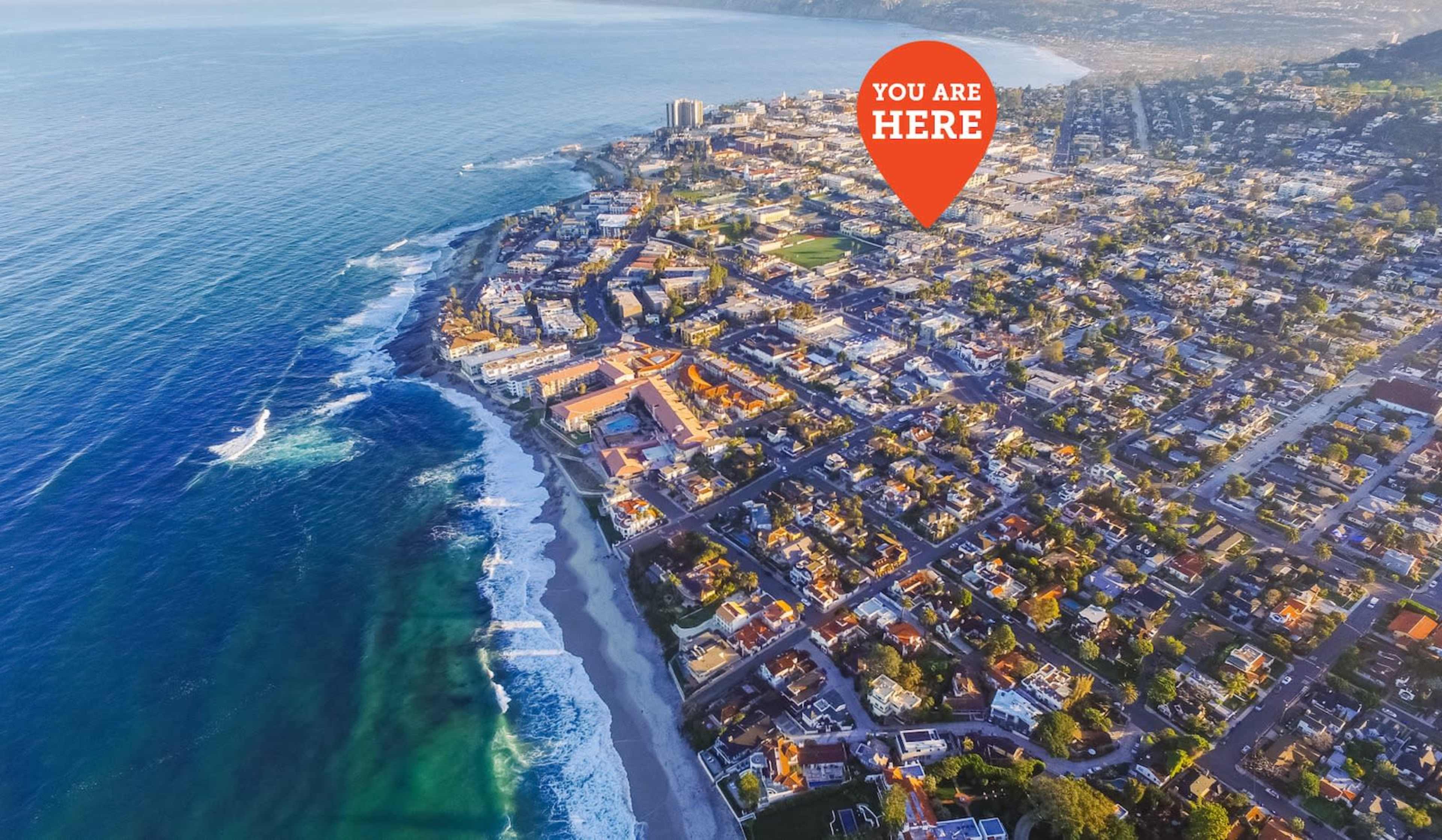 The image shows a coastal aerial view of a city with residential buildings and a beach along the shoreline.