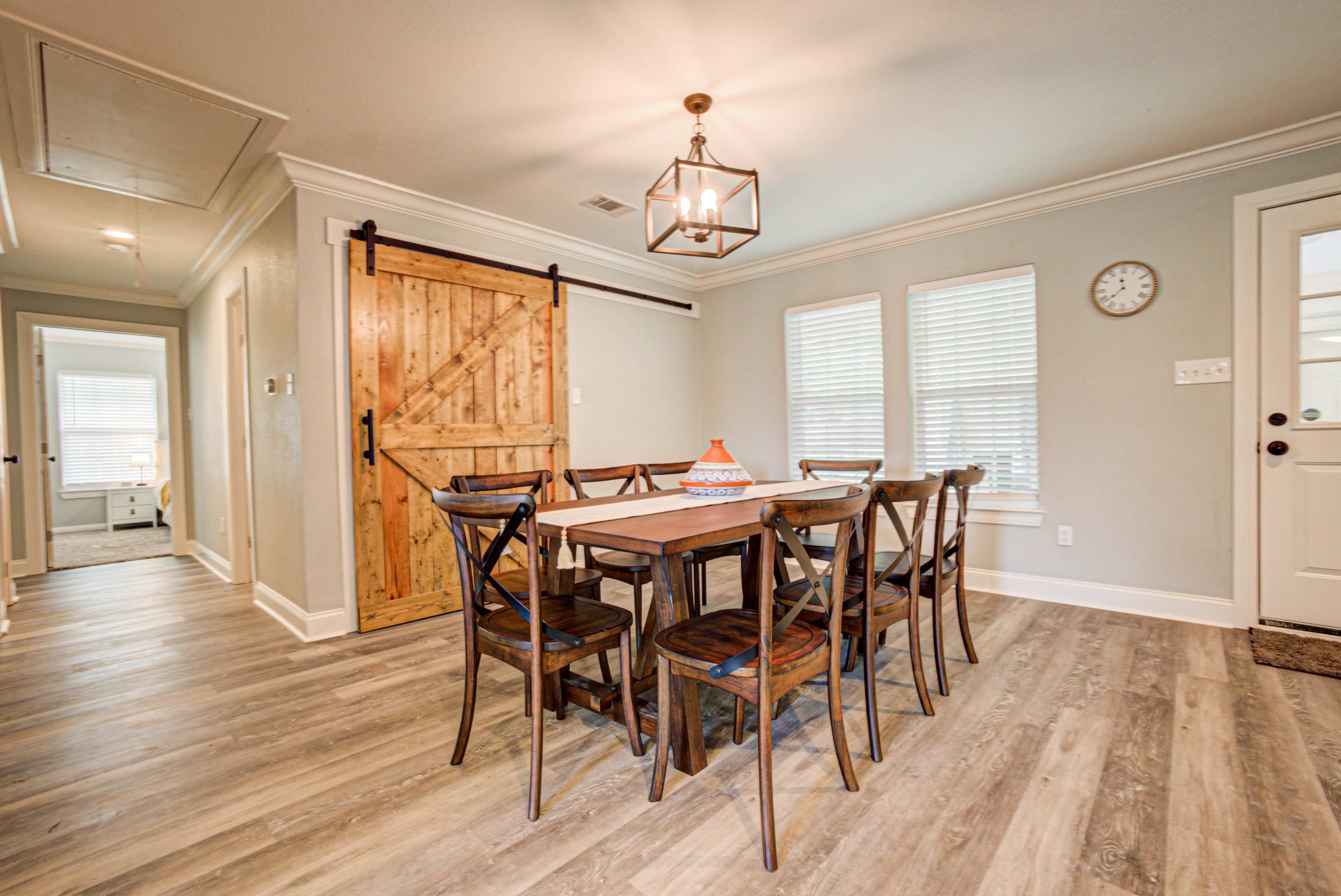 A dining area features a wooden table surrounded by six chairs, with a barn-style door and large windows allowing natural light.