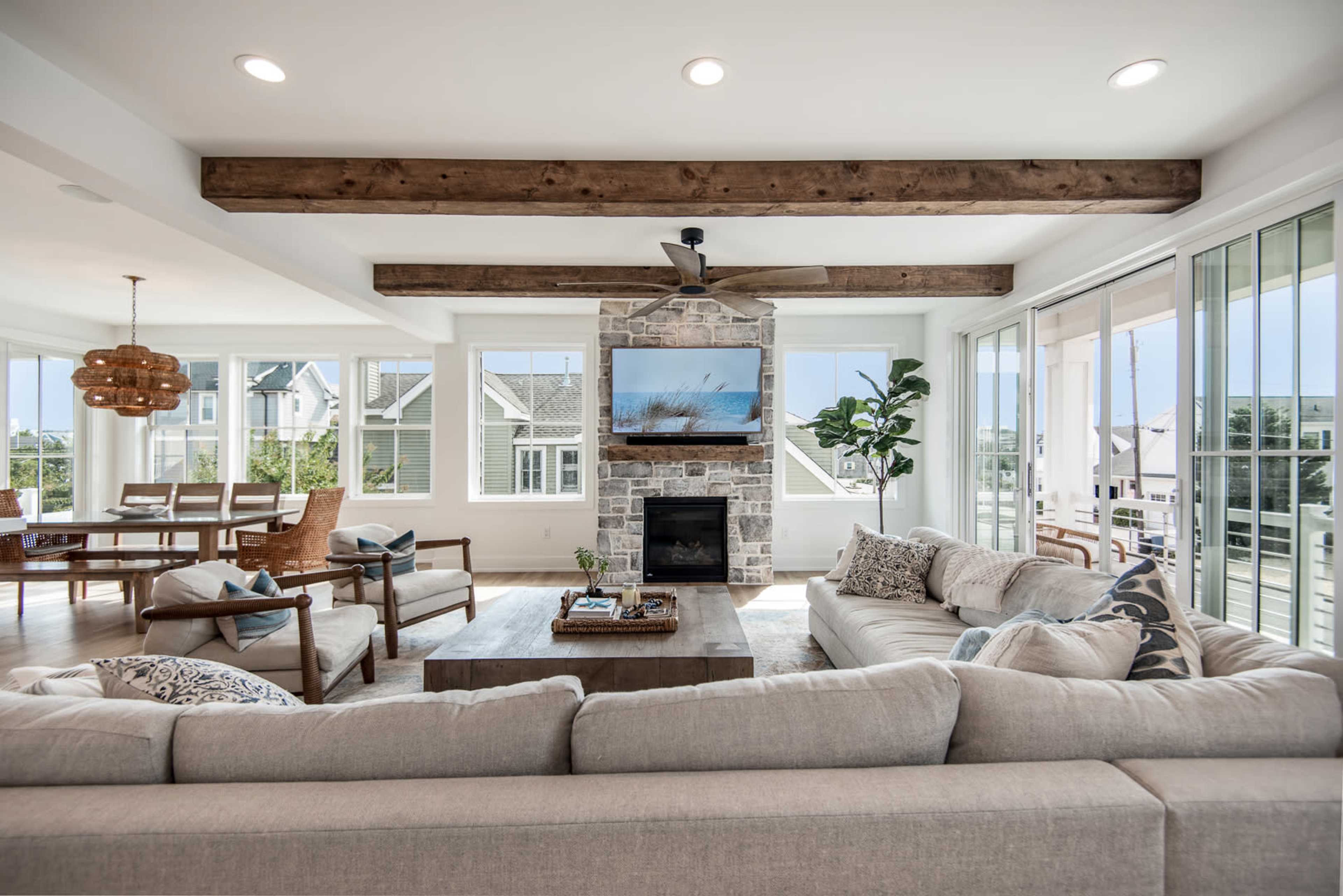 A modern living room with a stone fireplace, large windows, wooden beams, and a comfortable sectional sofa.