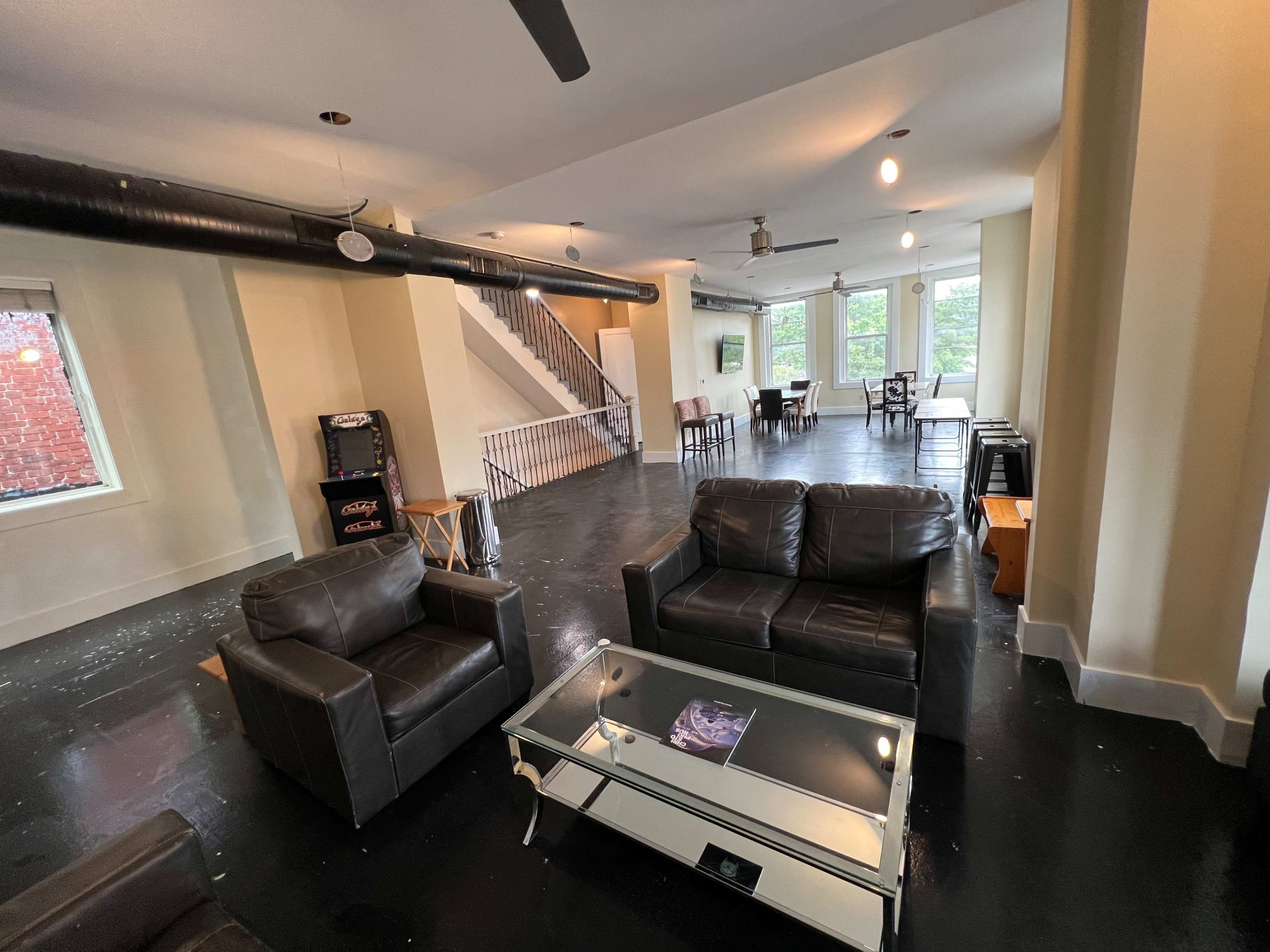 A spacious living area with black furniture, a glass coffee table, and a staircase leading to a second floor.
