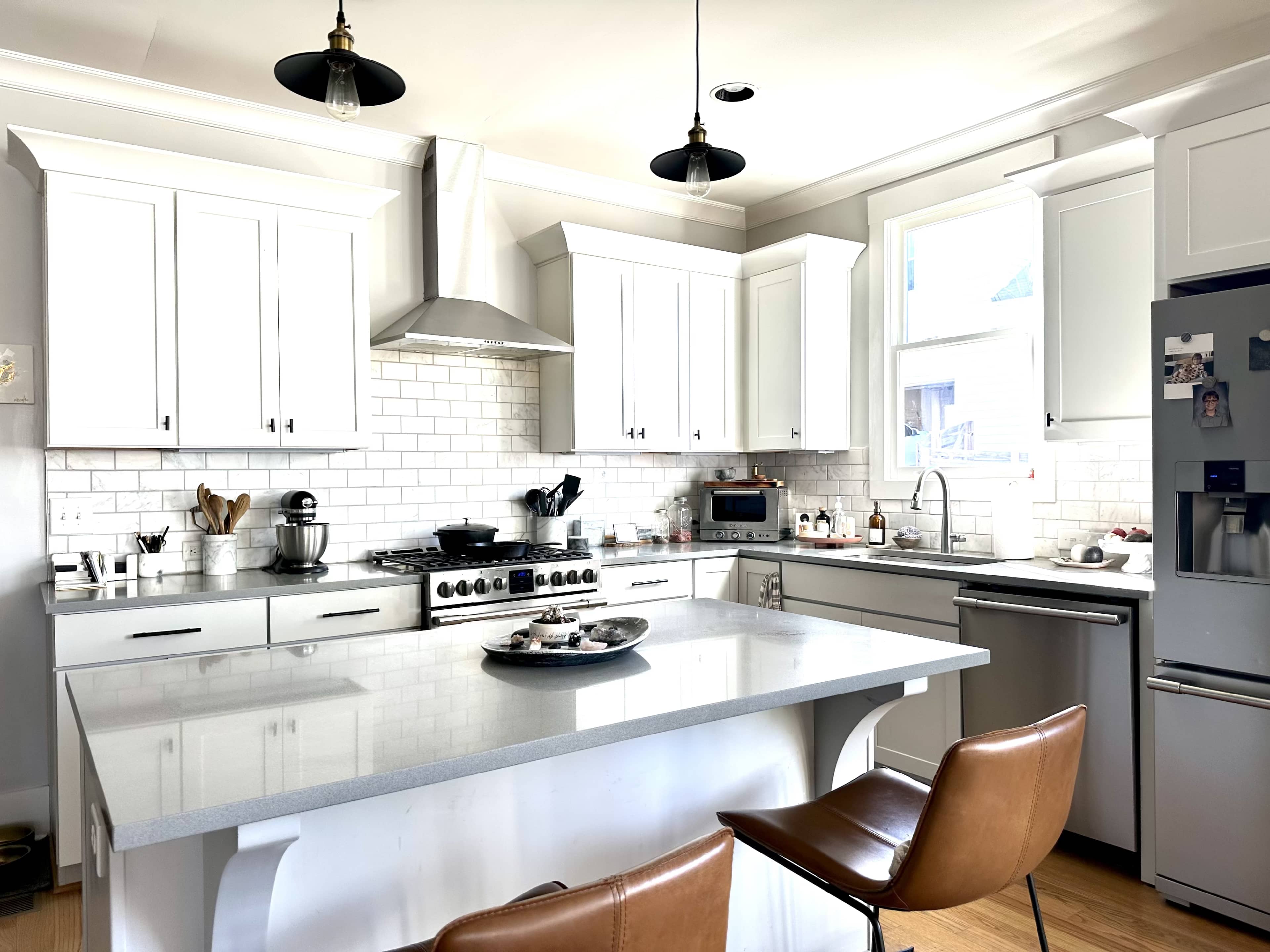 A modern kitchen features white cabinetry, a stainless steel refrigerator, and a large island with leather bar stools.