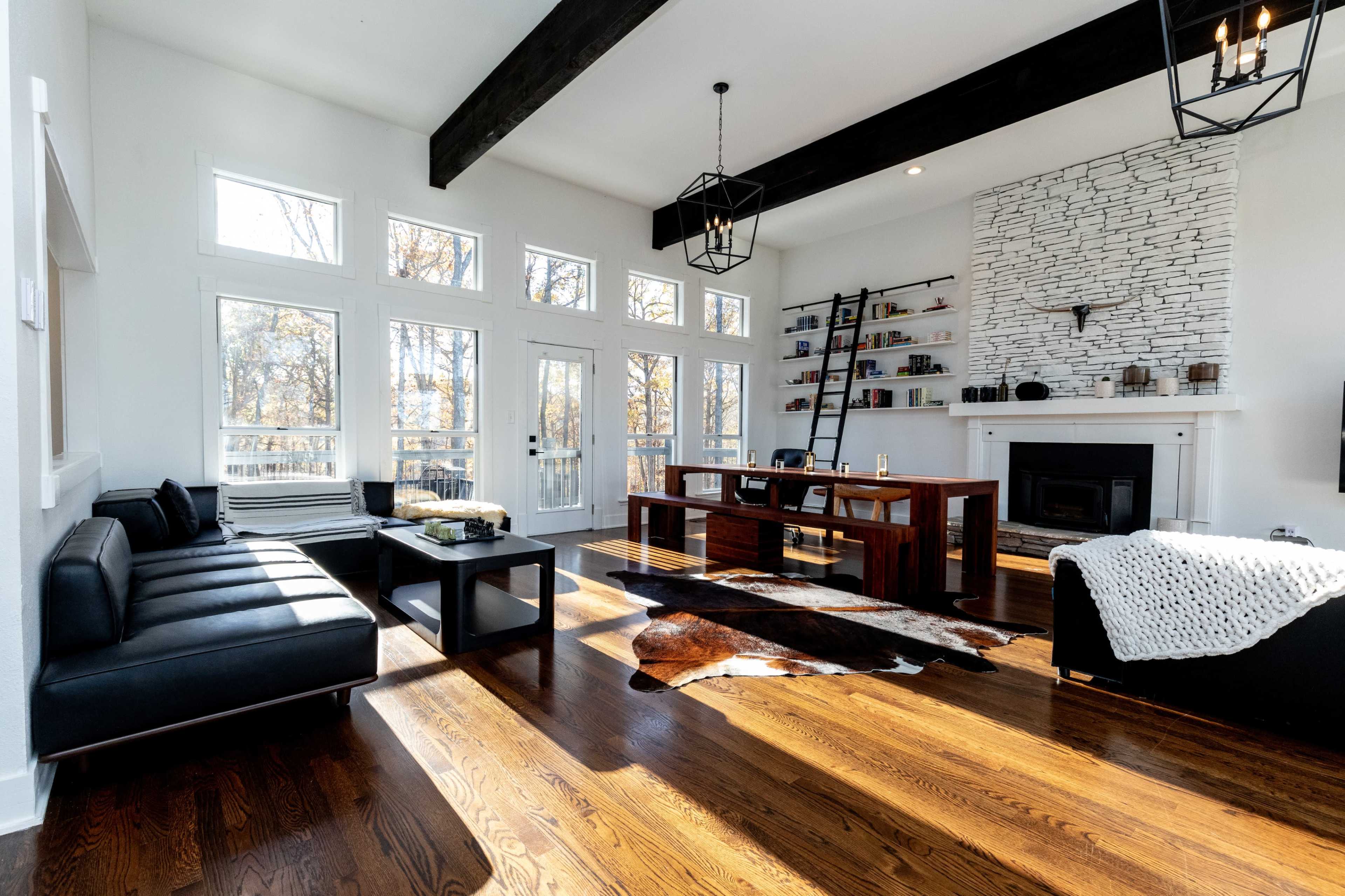 The living room features a black leather sofa, a wooden table, and a white stone fireplace, all complemented by large windows that allow natural light to fill the space.