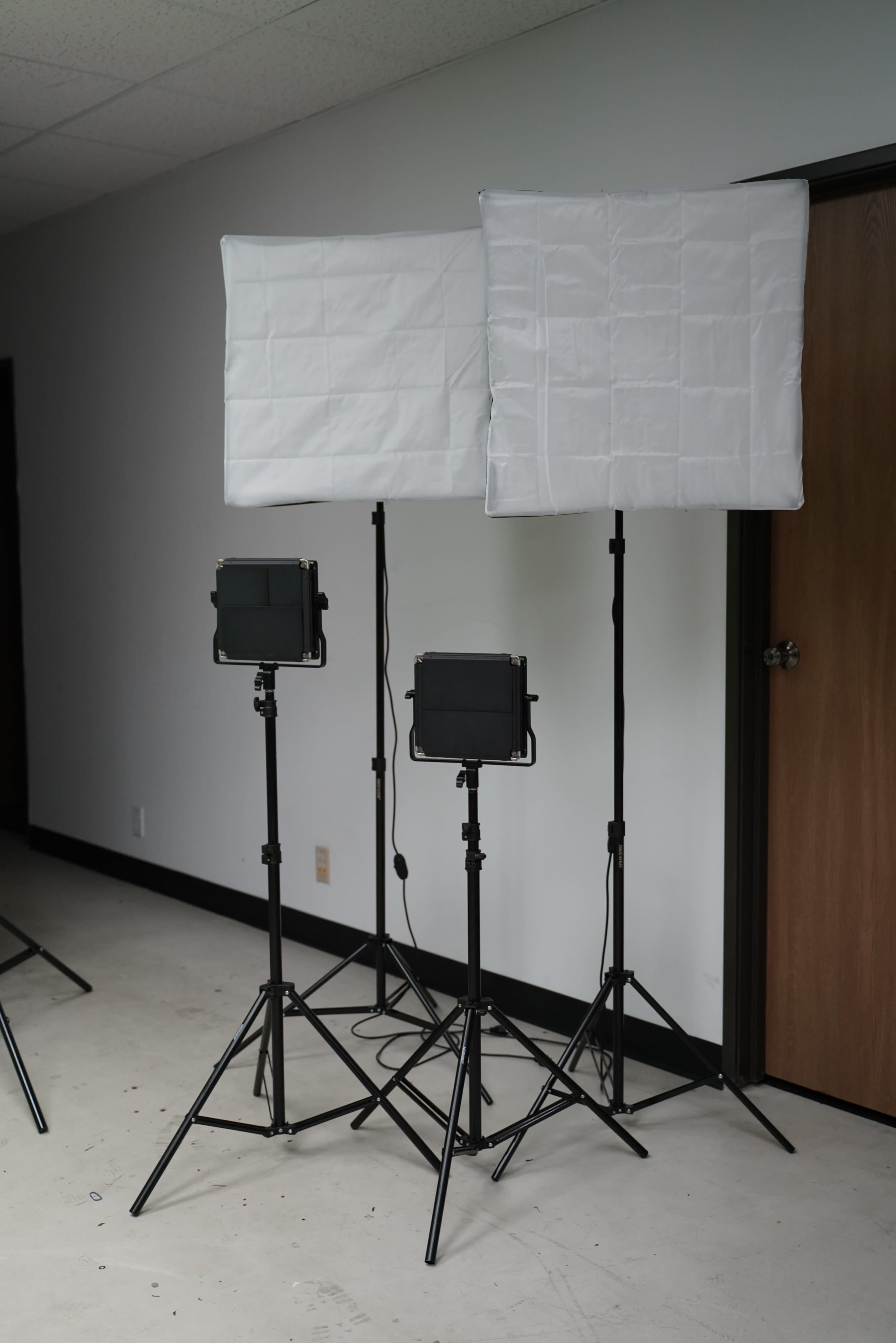Two softbox lights and one LED panel light on stands in a room with a door in the background.