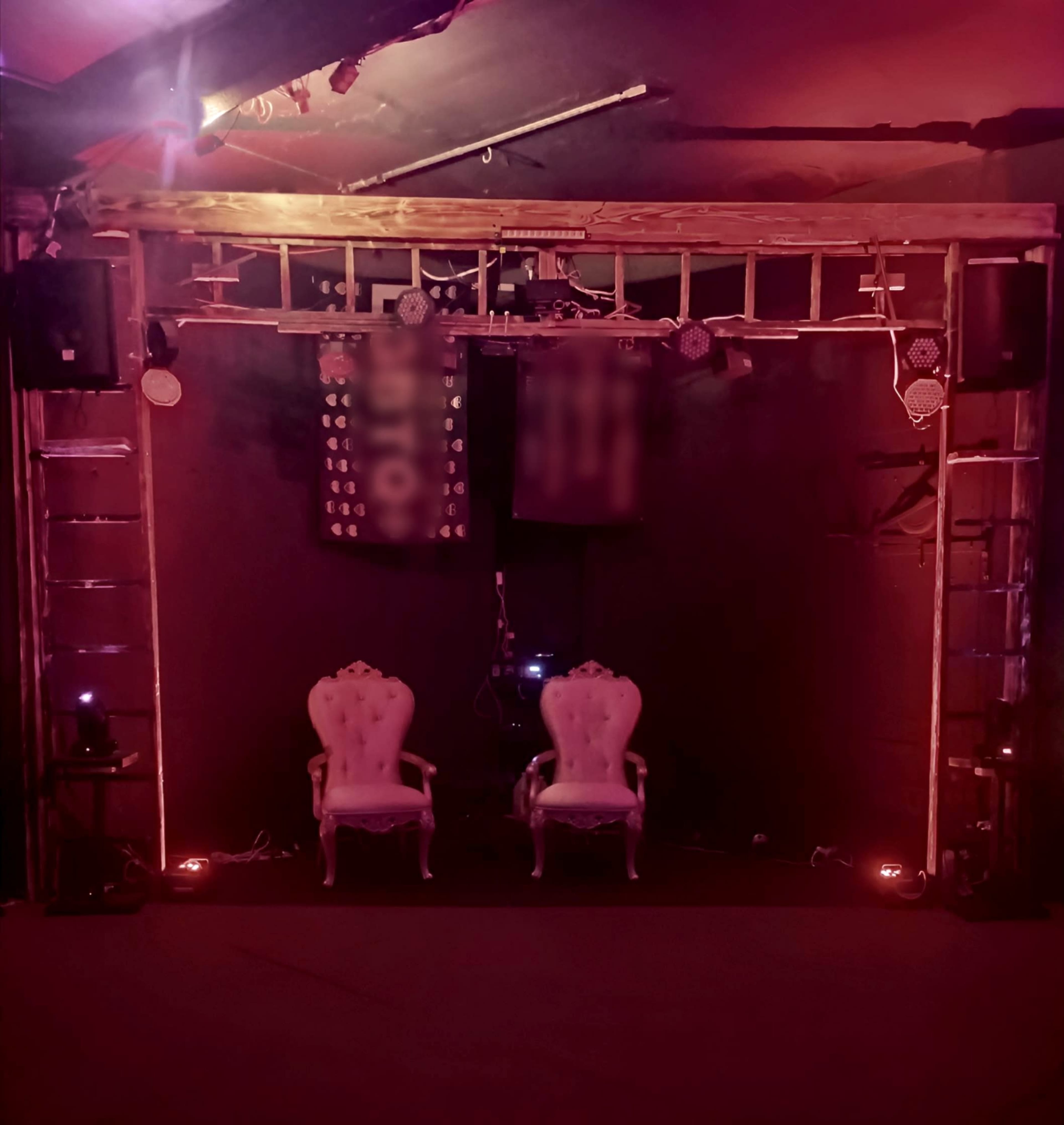 The image shows an empty stage setup with two ornate chairs in front of a backdrop featuring lights and sound equipment.