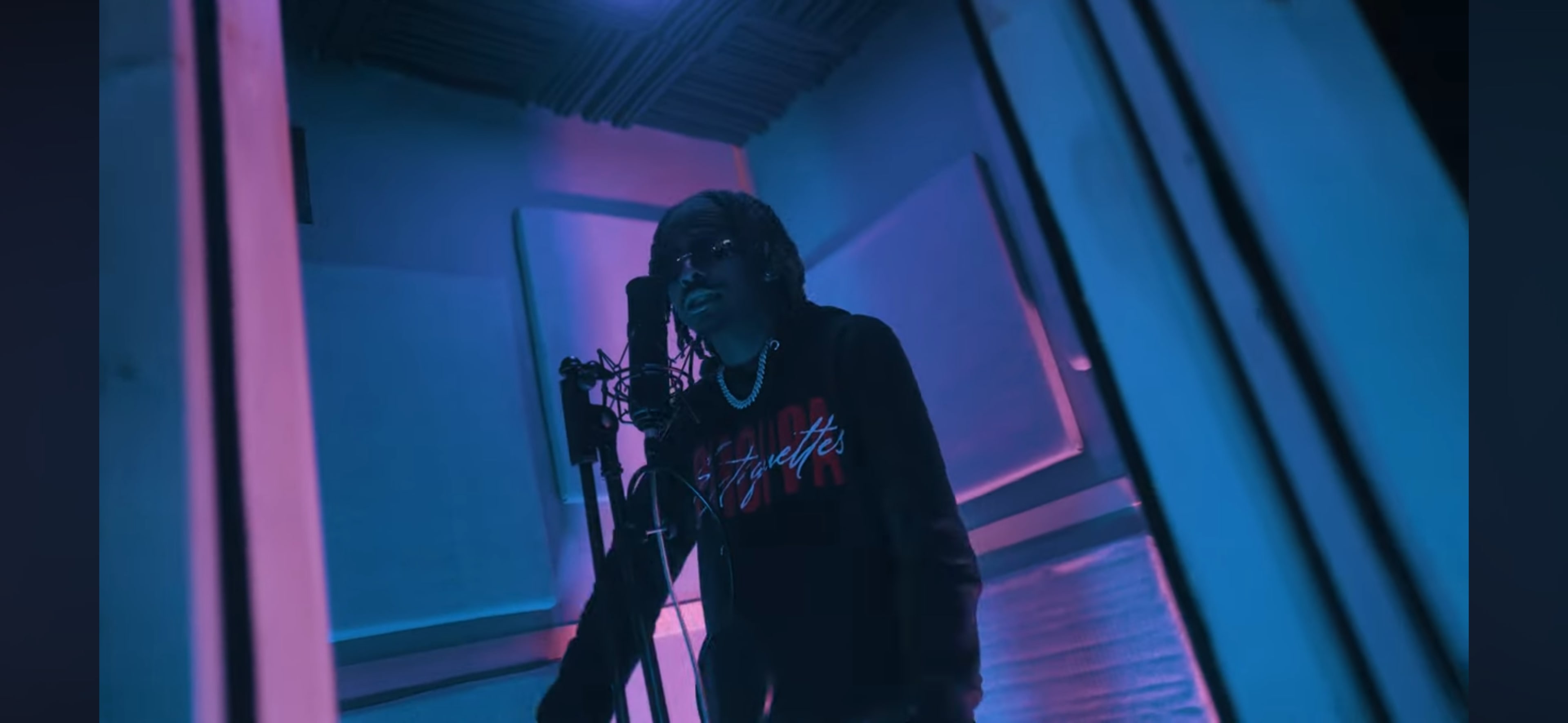 A person stands in a soundproof recording studio, microphone in front, surrounded by colorful ambient lighting.