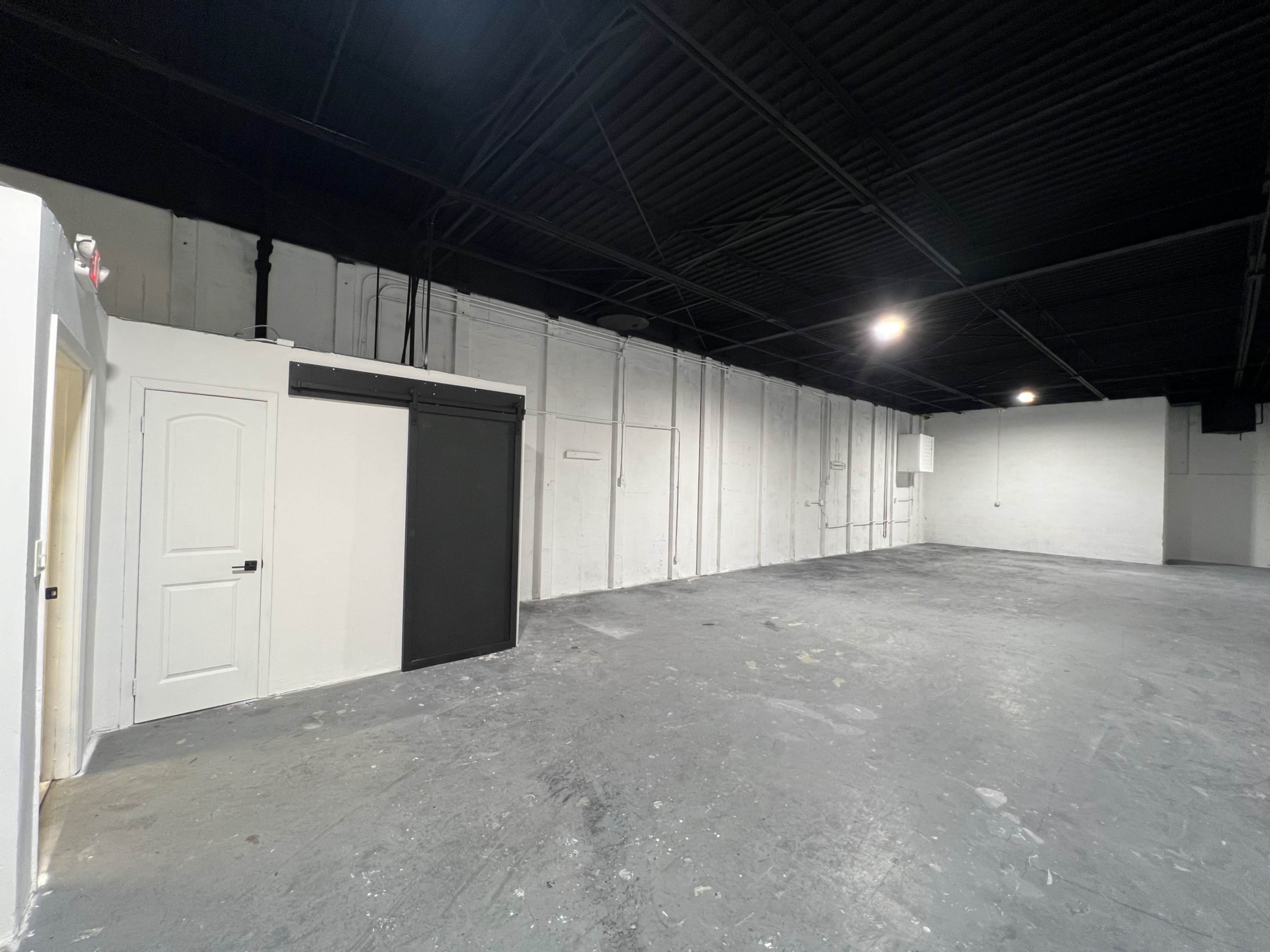 The image shows a spacious, empty industrial room with concrete flooring and a door on one side.
