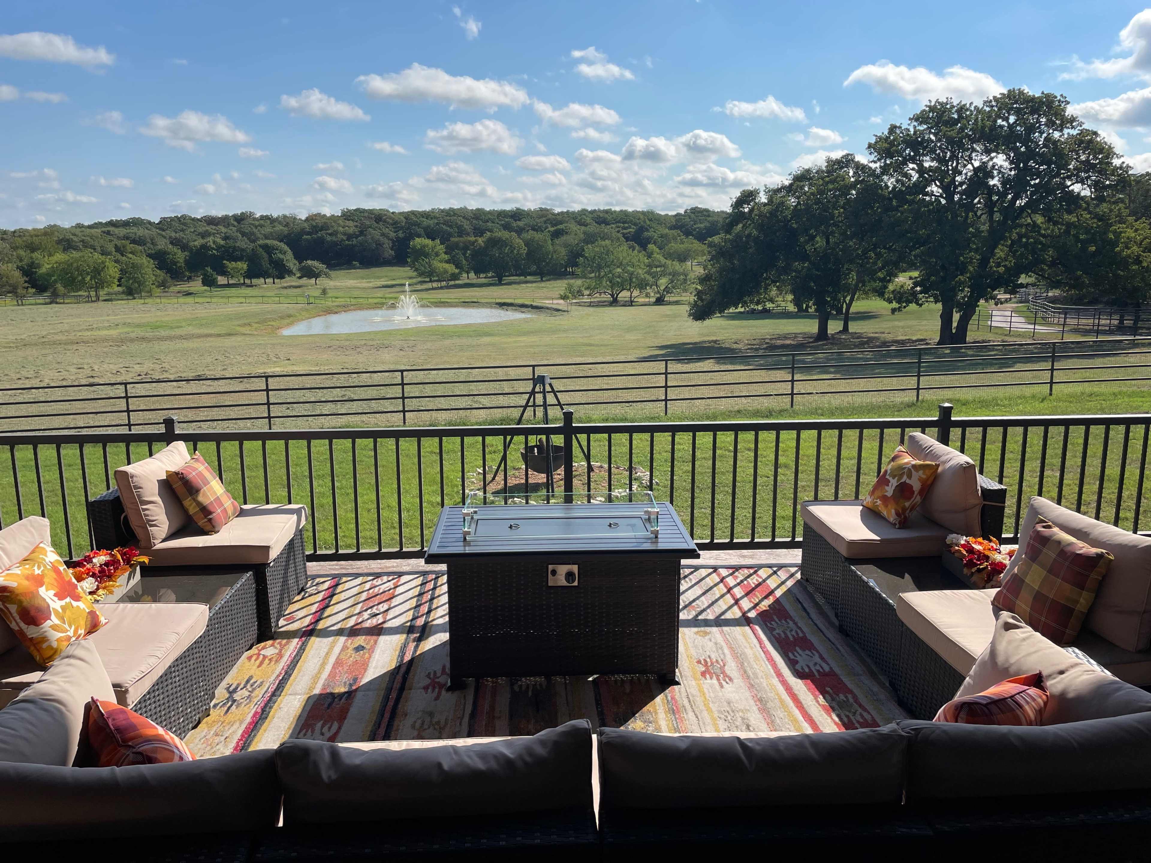 A patio with seating and a coffee table overlooks a grassy landscape and a small pond.