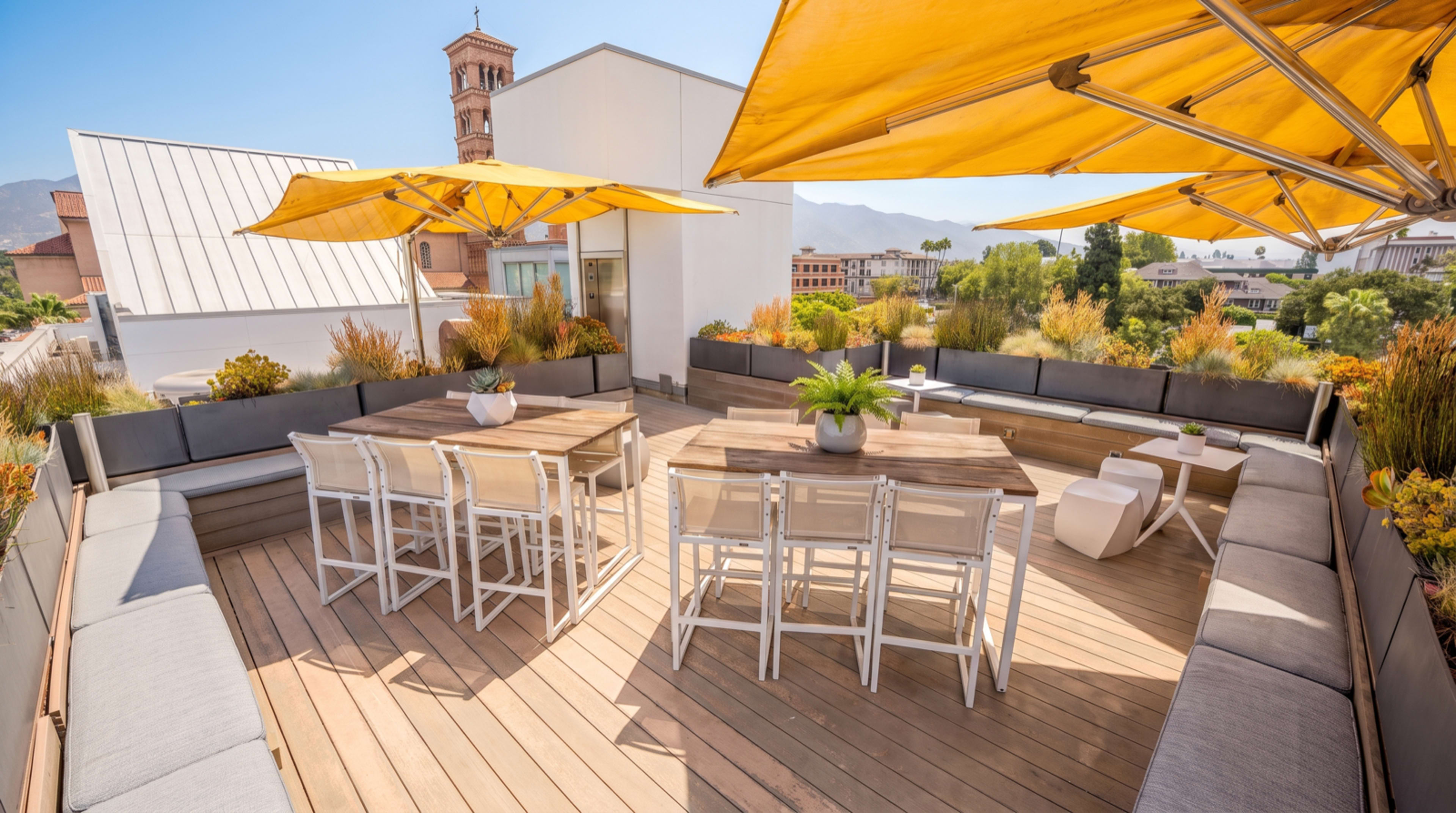 The image shows a spacious rooftop terrace with wooden flooring, a large dining table, and yellow umbrellas providing shade.