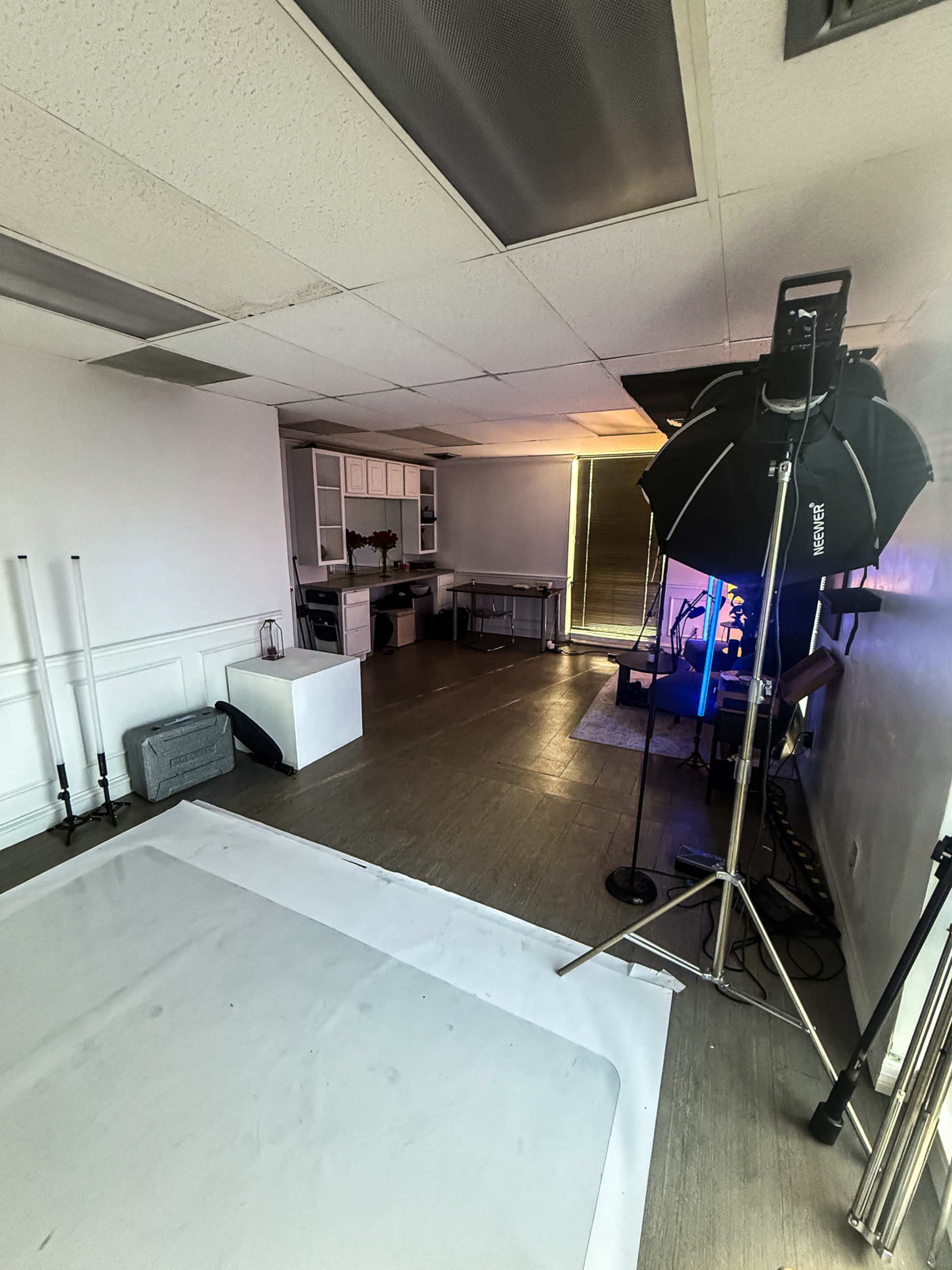 The image shows a photography studio with a backdrop, lighting equipment, and a work area containing a table and chairs.