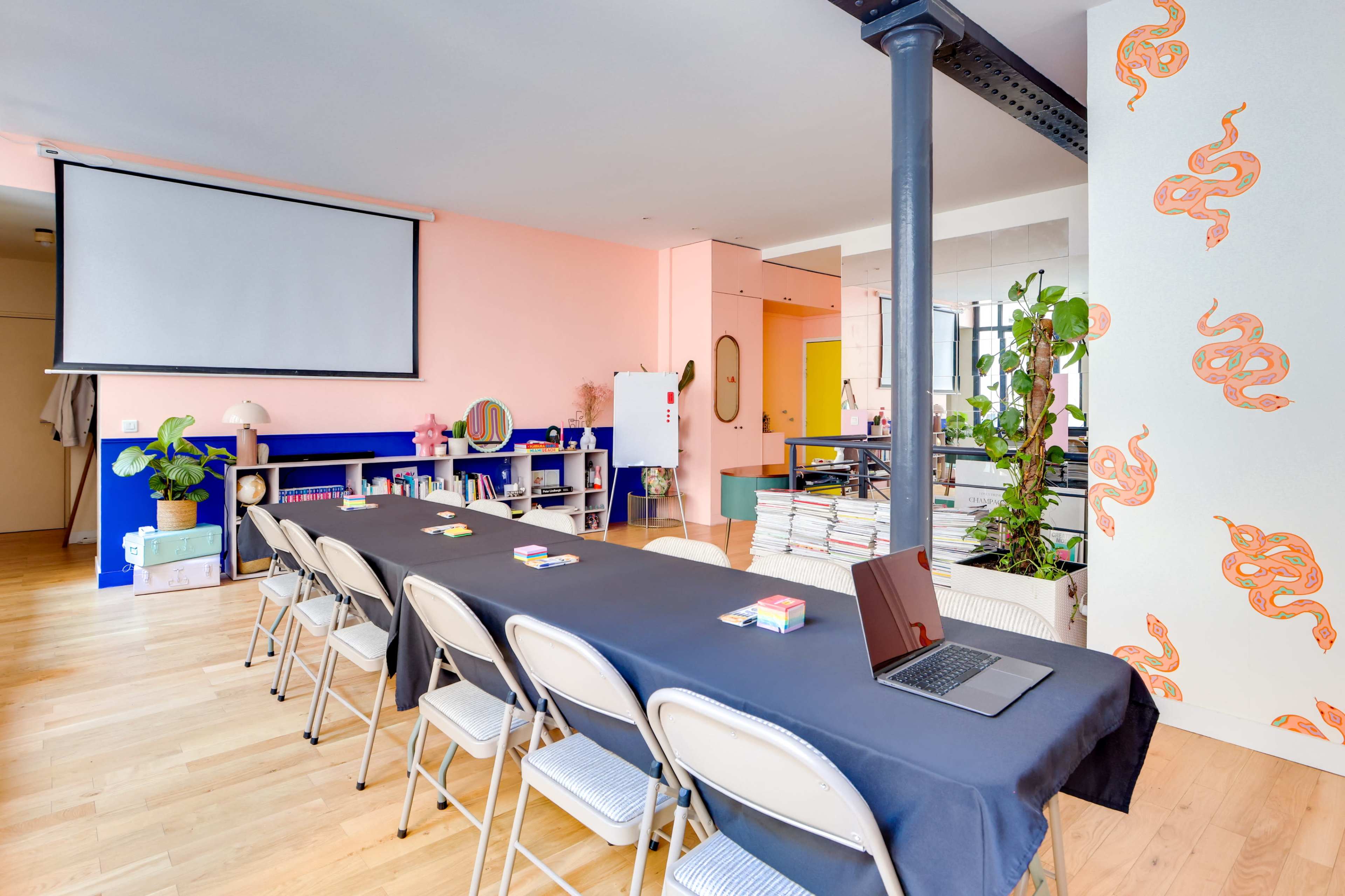 The image shows a modern, well-lit meeting space with a long table covered in a black tablecloth and equipped with chairs, a laptop, and various decorative elements.