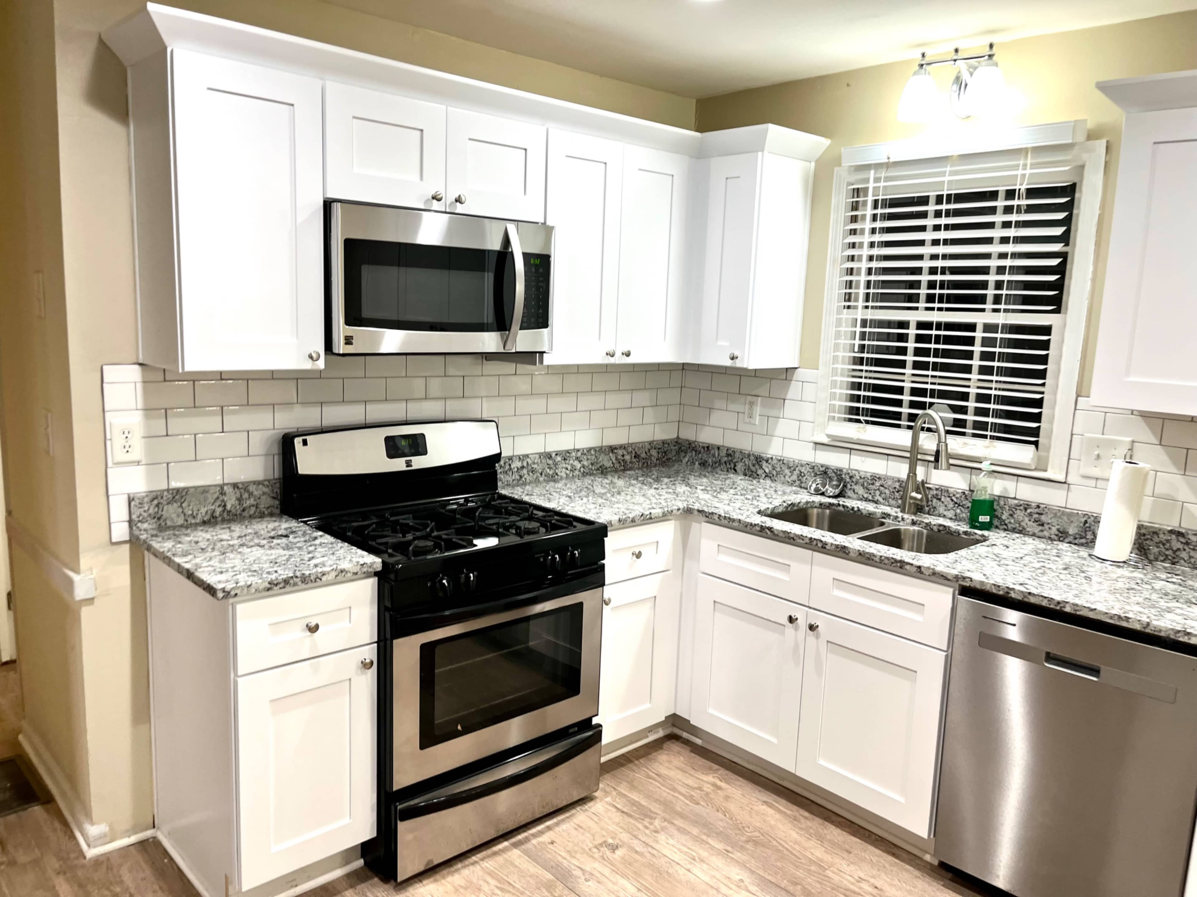 A modern kitchen features white cabinets, a stainless steel microwave and stove, granite countertops, a double sink, and a silver dishwasher.