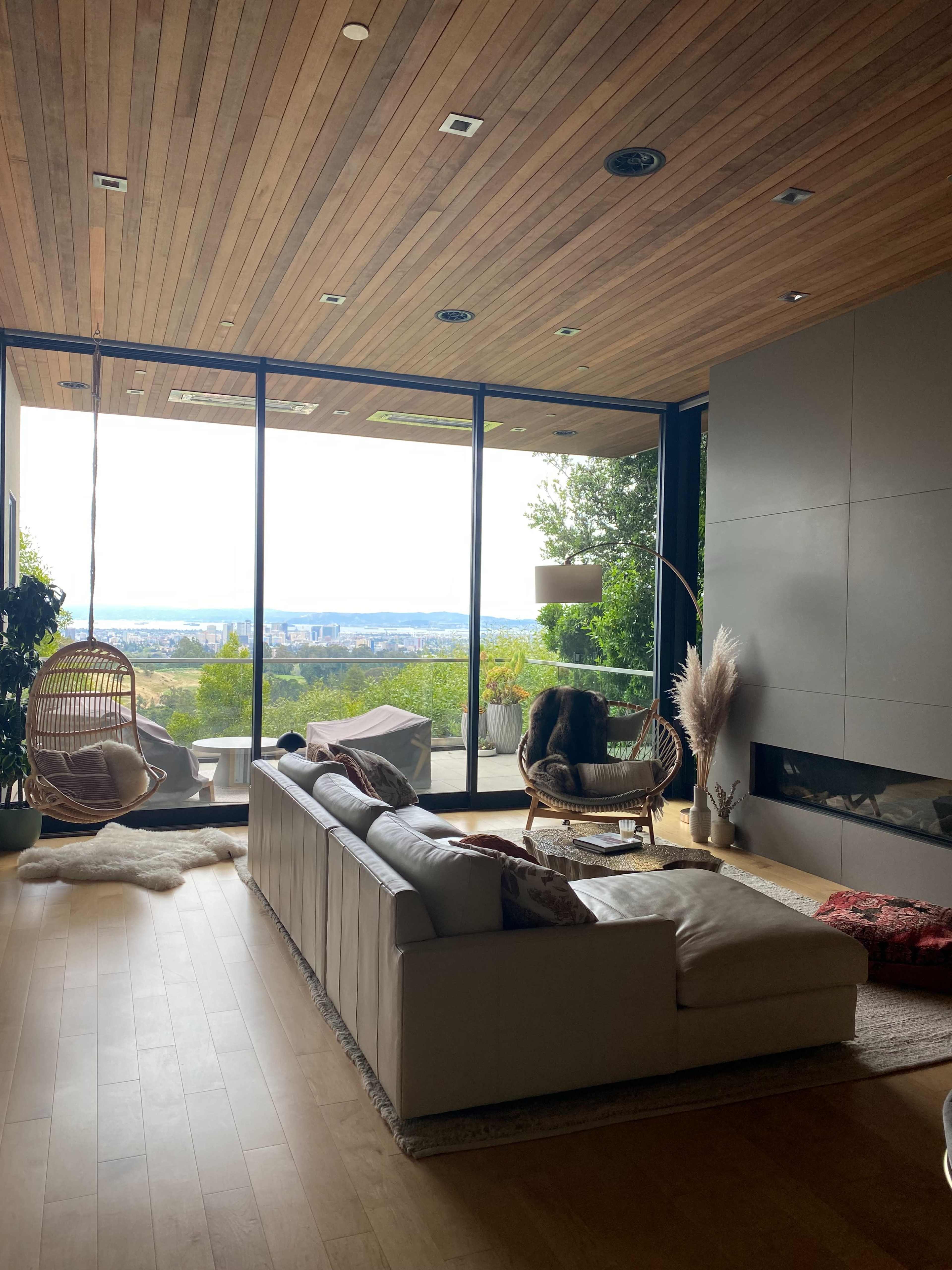 A modern living room with a large window overlooking a scenic view, featuring a sectional sofa, a hanging chair, and a minimalist decor.