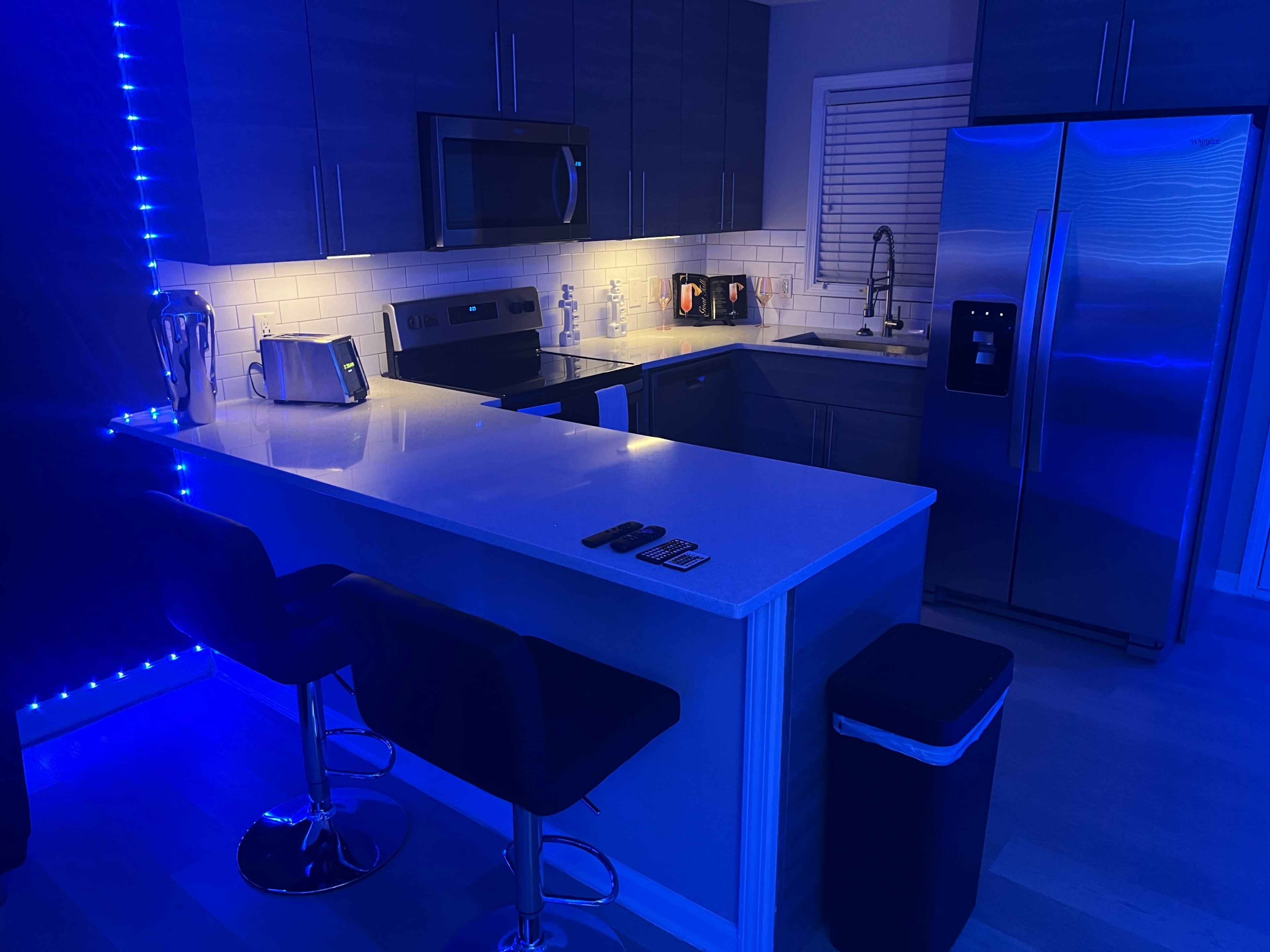 The image shows a modern kitchen with stainless steel appliances, blue LED lighting, and a sleek island with bar stools.
