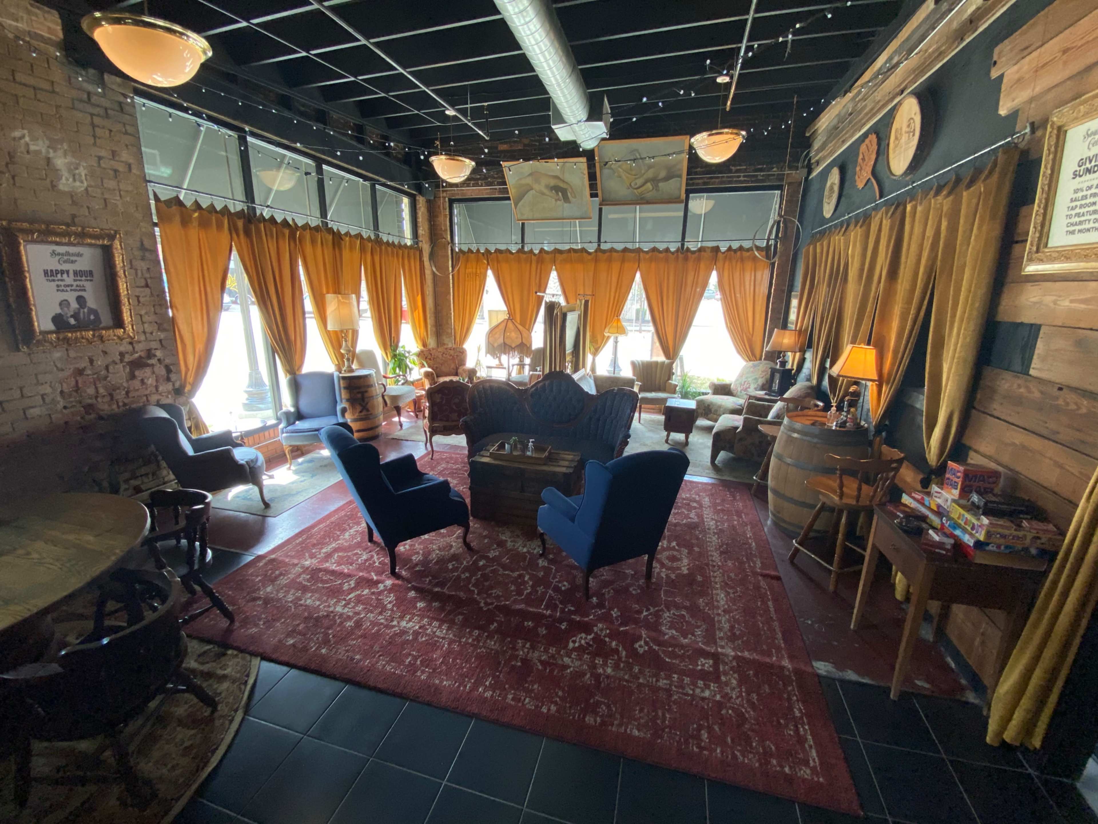 A cozy lounge area with plush blue chairs, wooden furniture, and large windows draped with orange curtains.