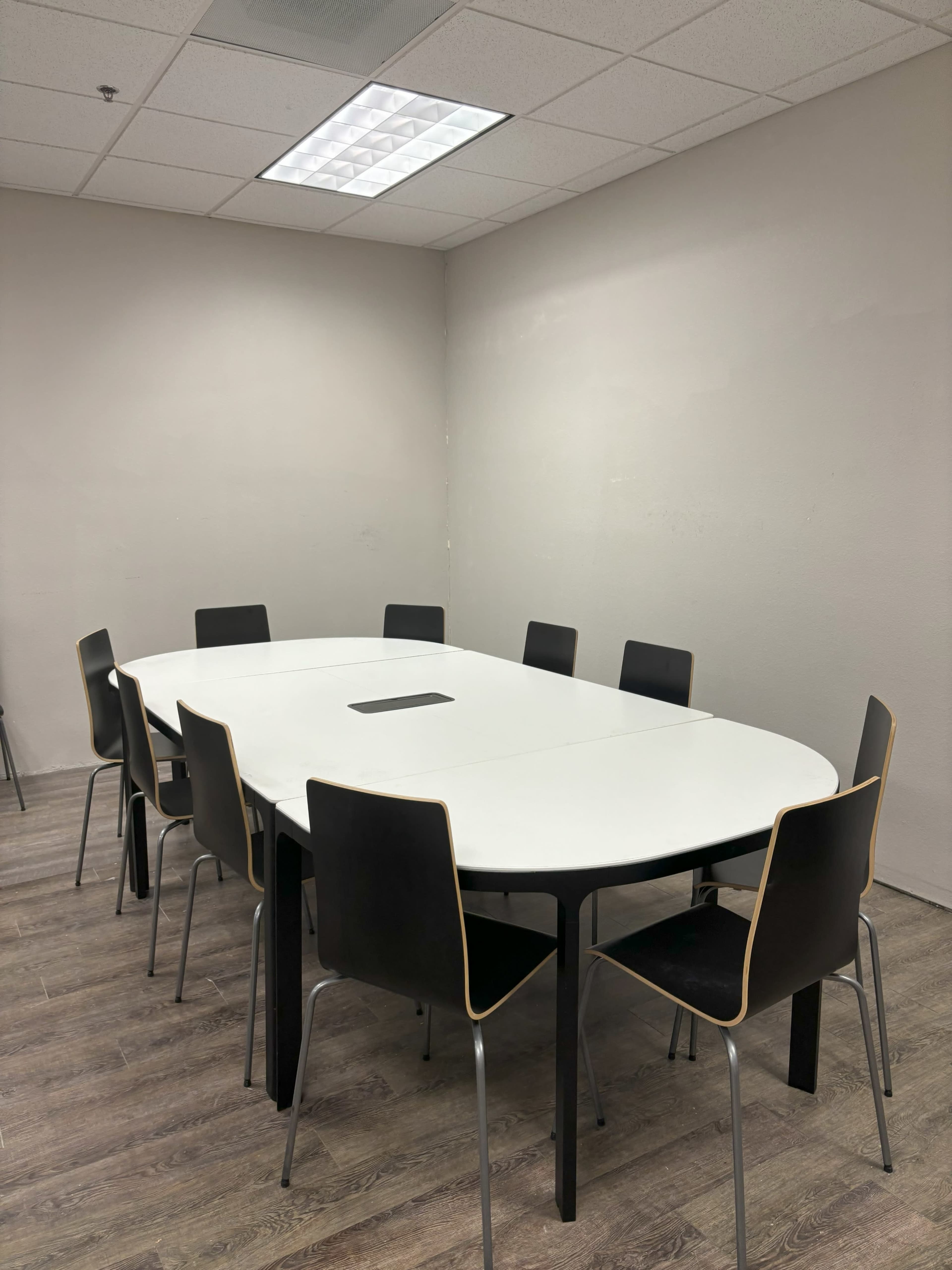 A conference room features a large white oval table surrounded by eight black chairs with wooden accents.