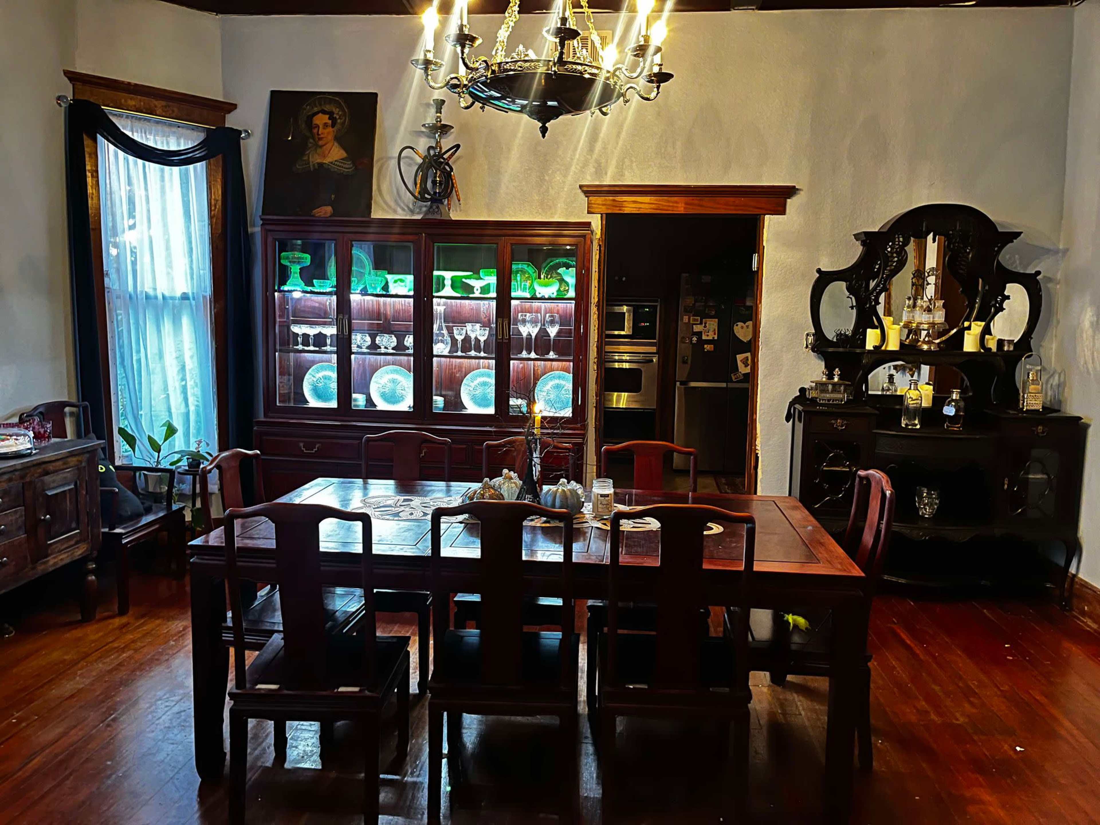 A wooden dining table surrounded by chairs is positioned in a room featuring a china cabinet, a vintage sideboard, and a chandelier.