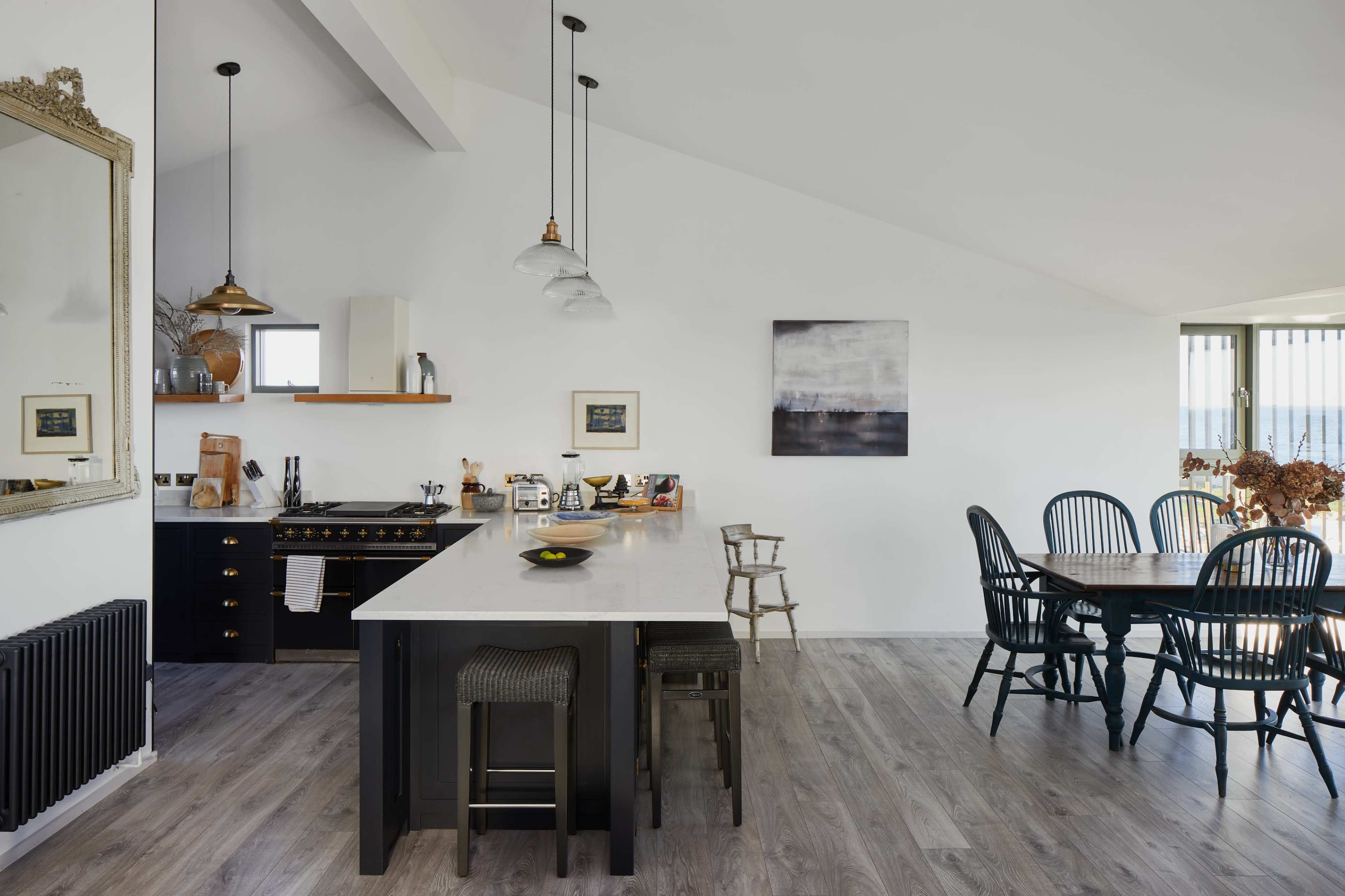 A modern kitchen and dining area feature a black and white color scheme with a large island, pendant lights, and a dining table set for six.