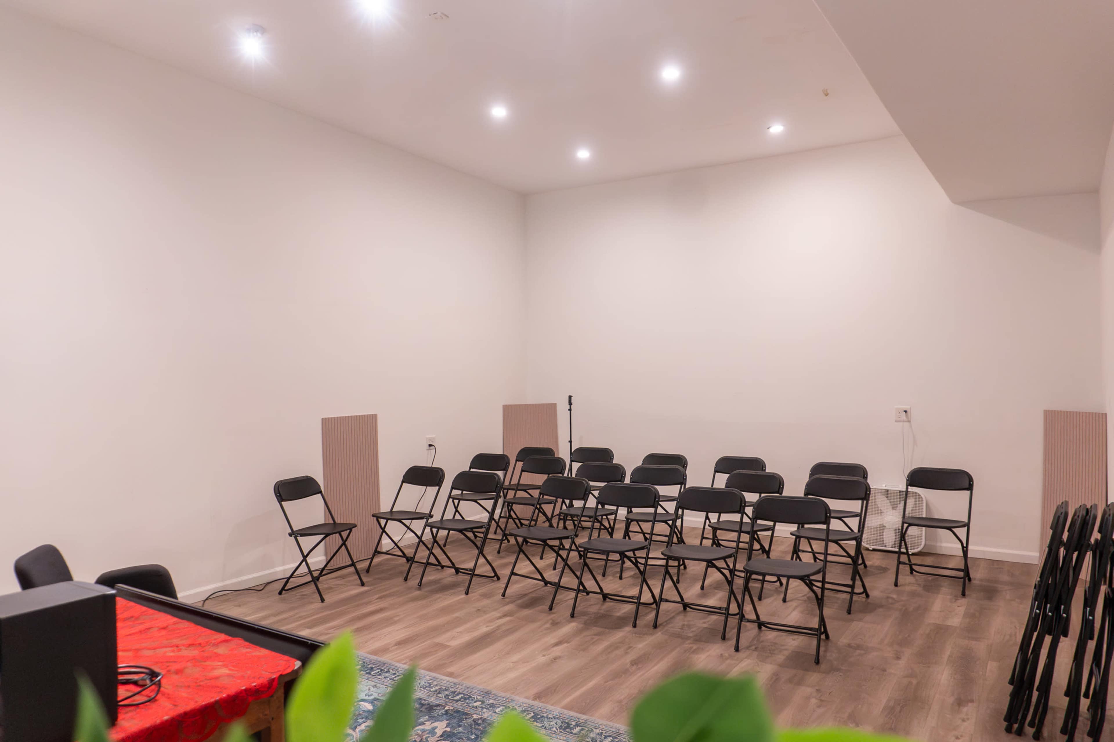The image shows a small, empty room with black folding chairs arranged in rows and a few chairs stacked against the wall.