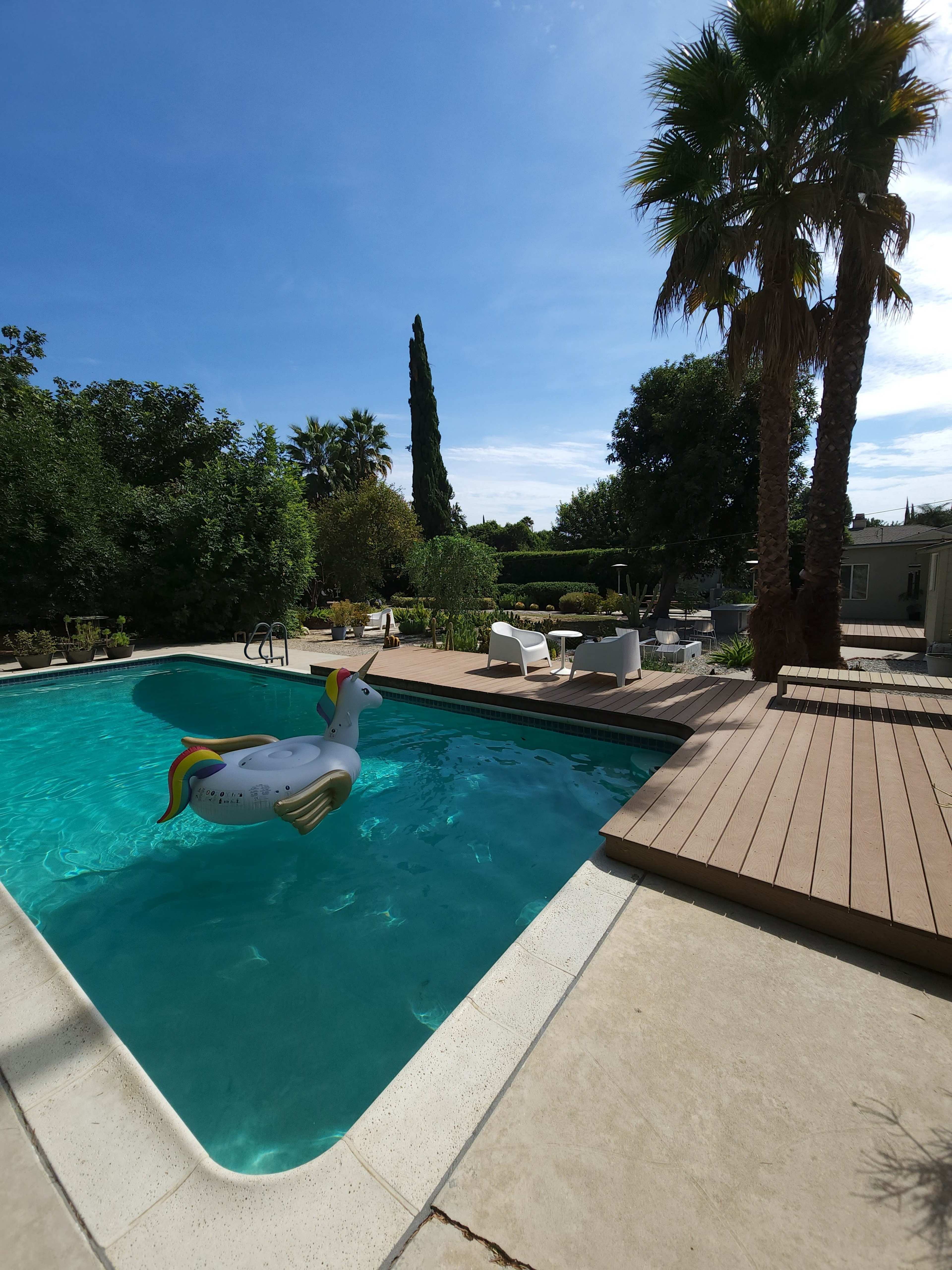 A unicorn-themed inflatable floats in a swimming pool surrounded by palm trees and outdoor seating.