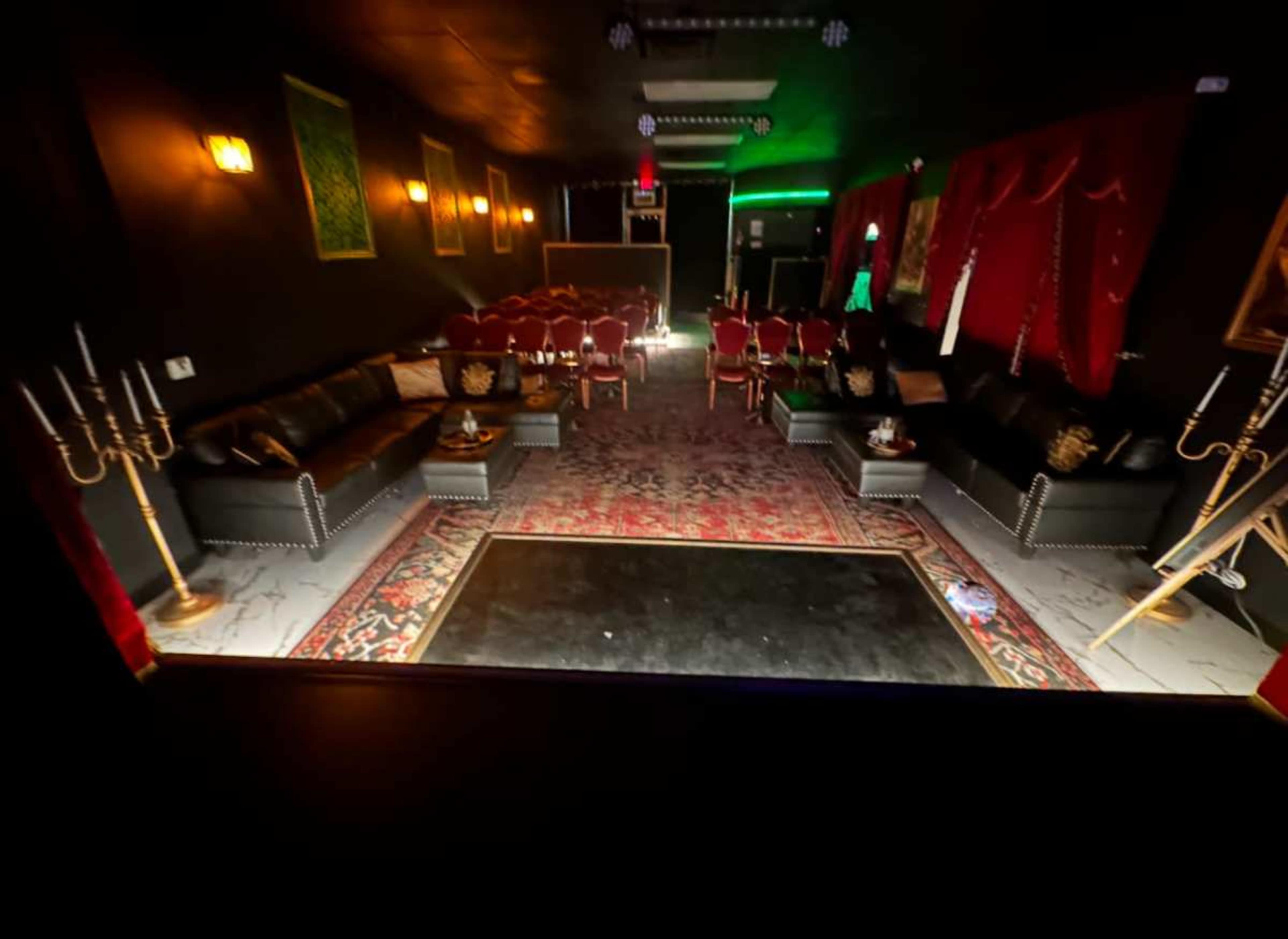 The image shows a dimly lit lounge with red curtains, seating arranged in rows, and decorative candelabras.