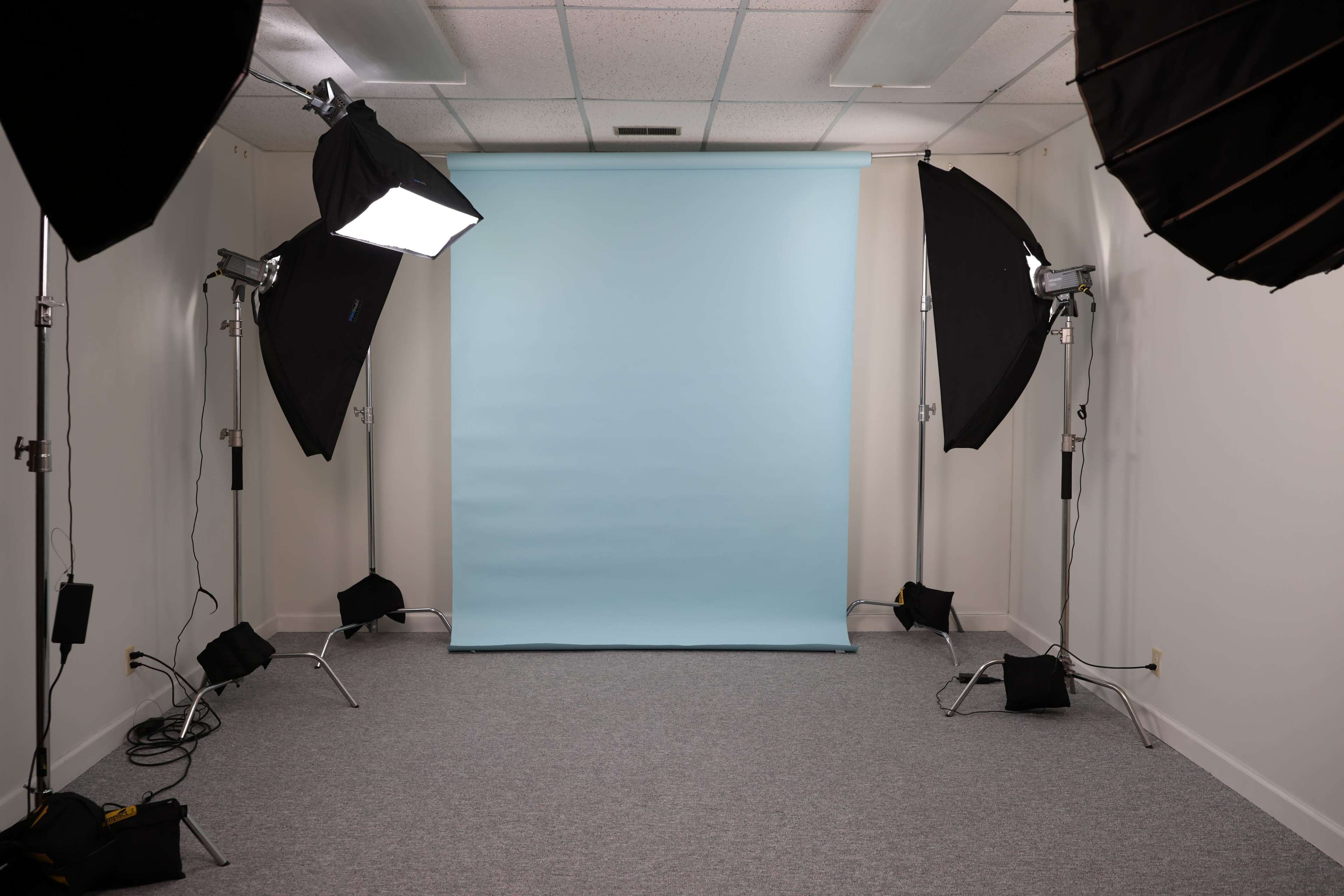 A photography studio features a light blue backdrop, surrounded by several softbox lighting setups on both sides.